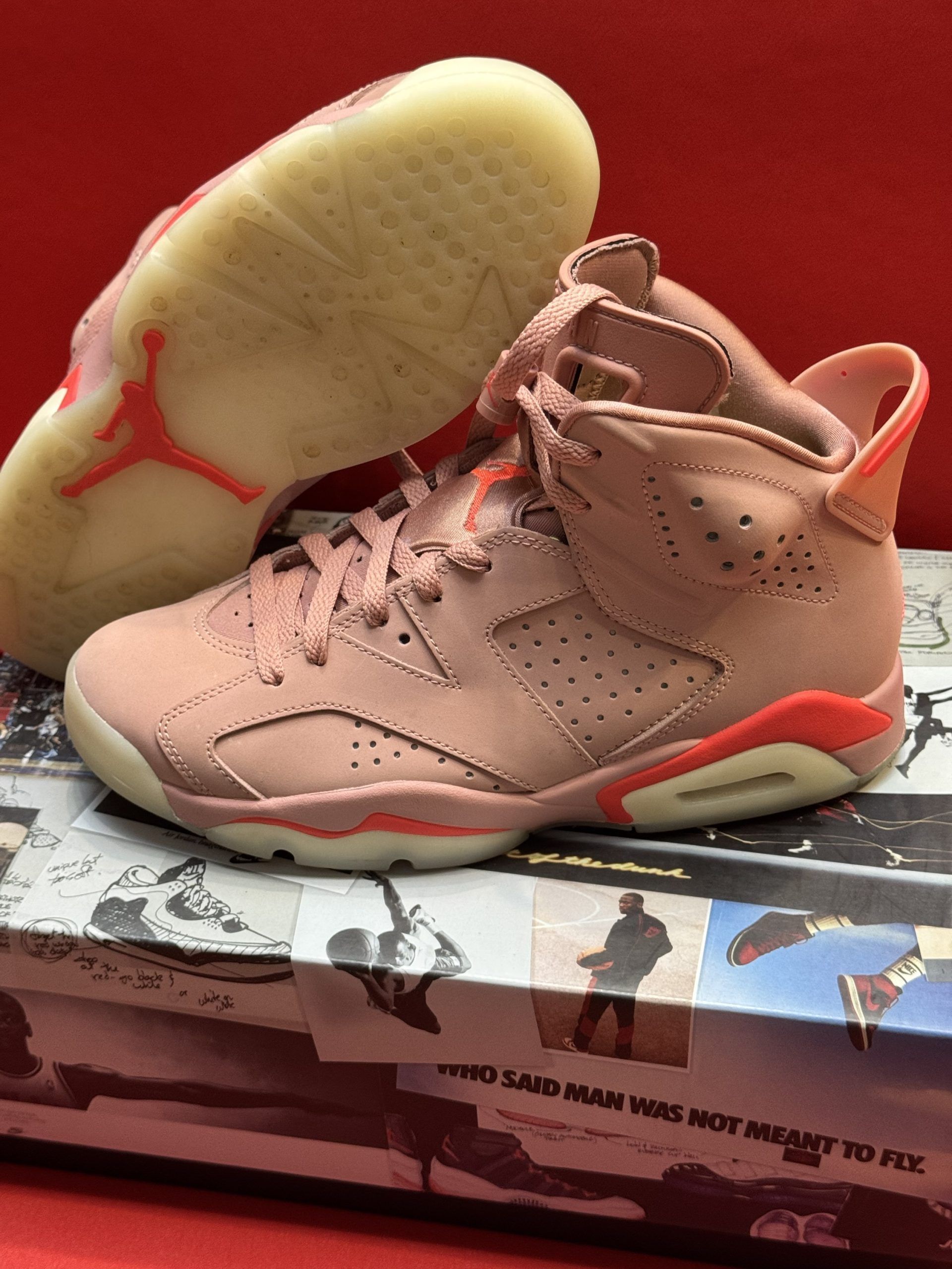 Pink Air Jordan 6 sneakers on a printed box, with orange accents and a light-colored sole.