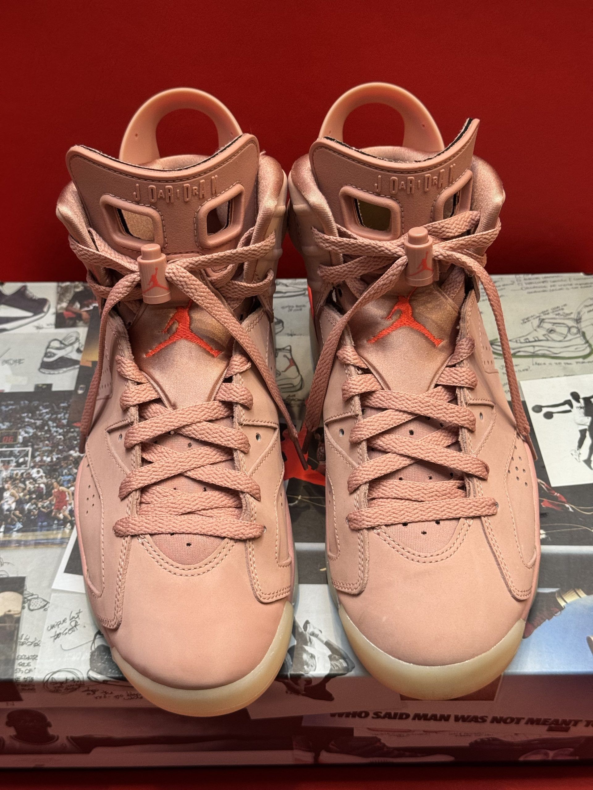 Pink Air Jordan 6 sneakers on a printed box, with orange accents and a light-colored sole.