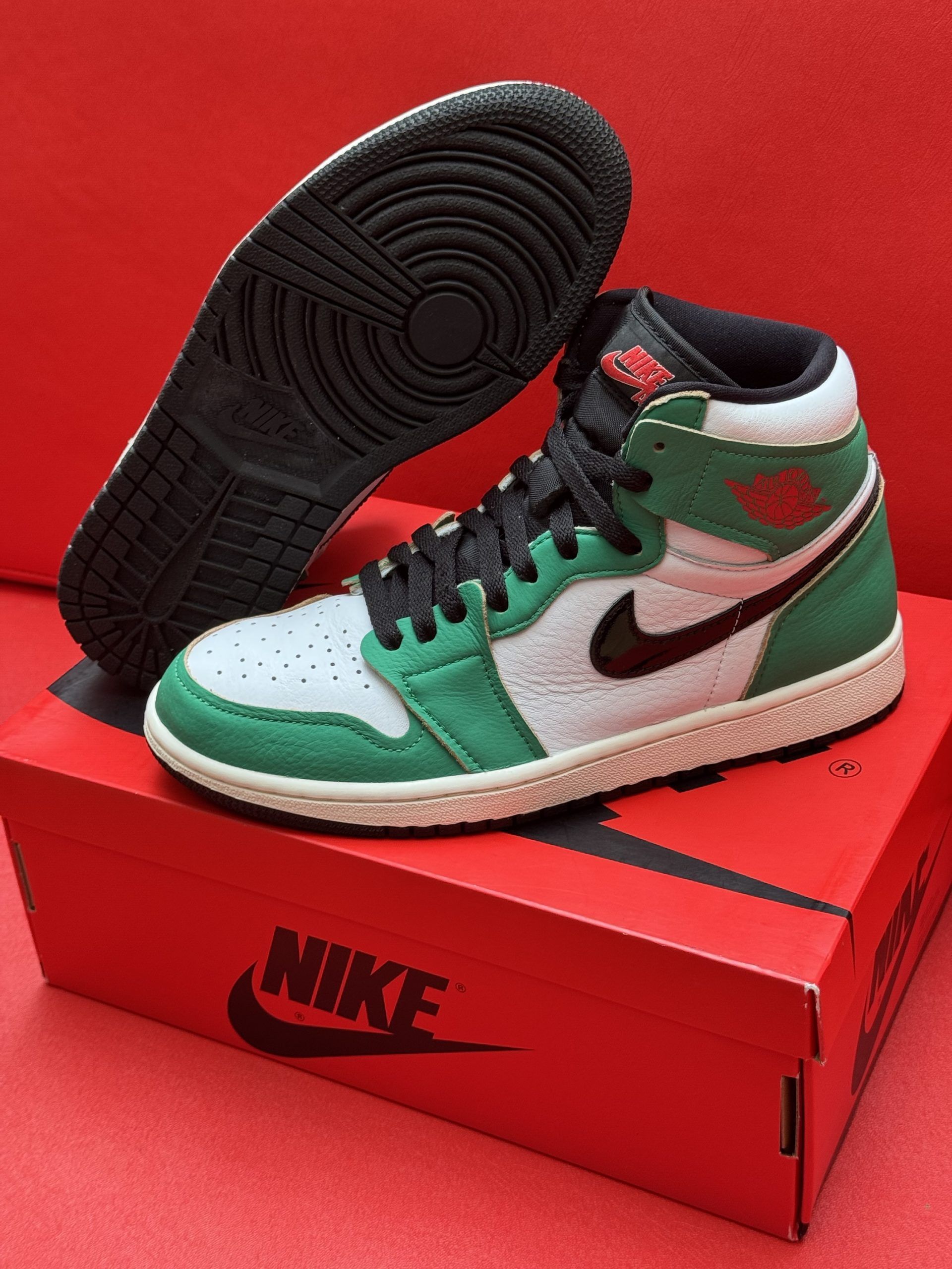 Green and white Air Jordan 1 sneaker on a red Nike box, with the black sole beside it.