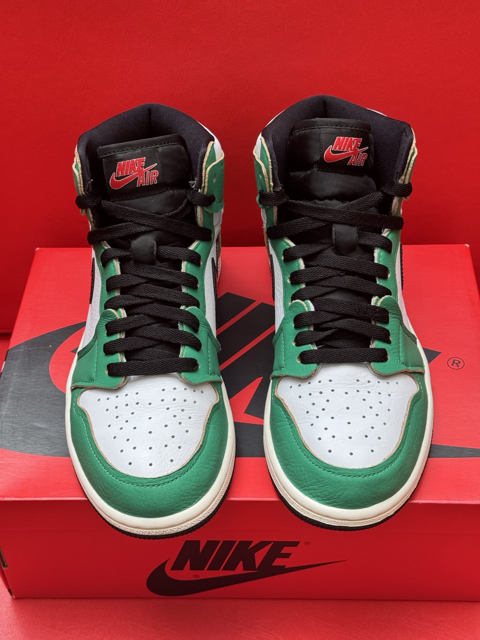 Green and white Air Jordan 1 sneaker on a red Nike box, with the black sole beside it.