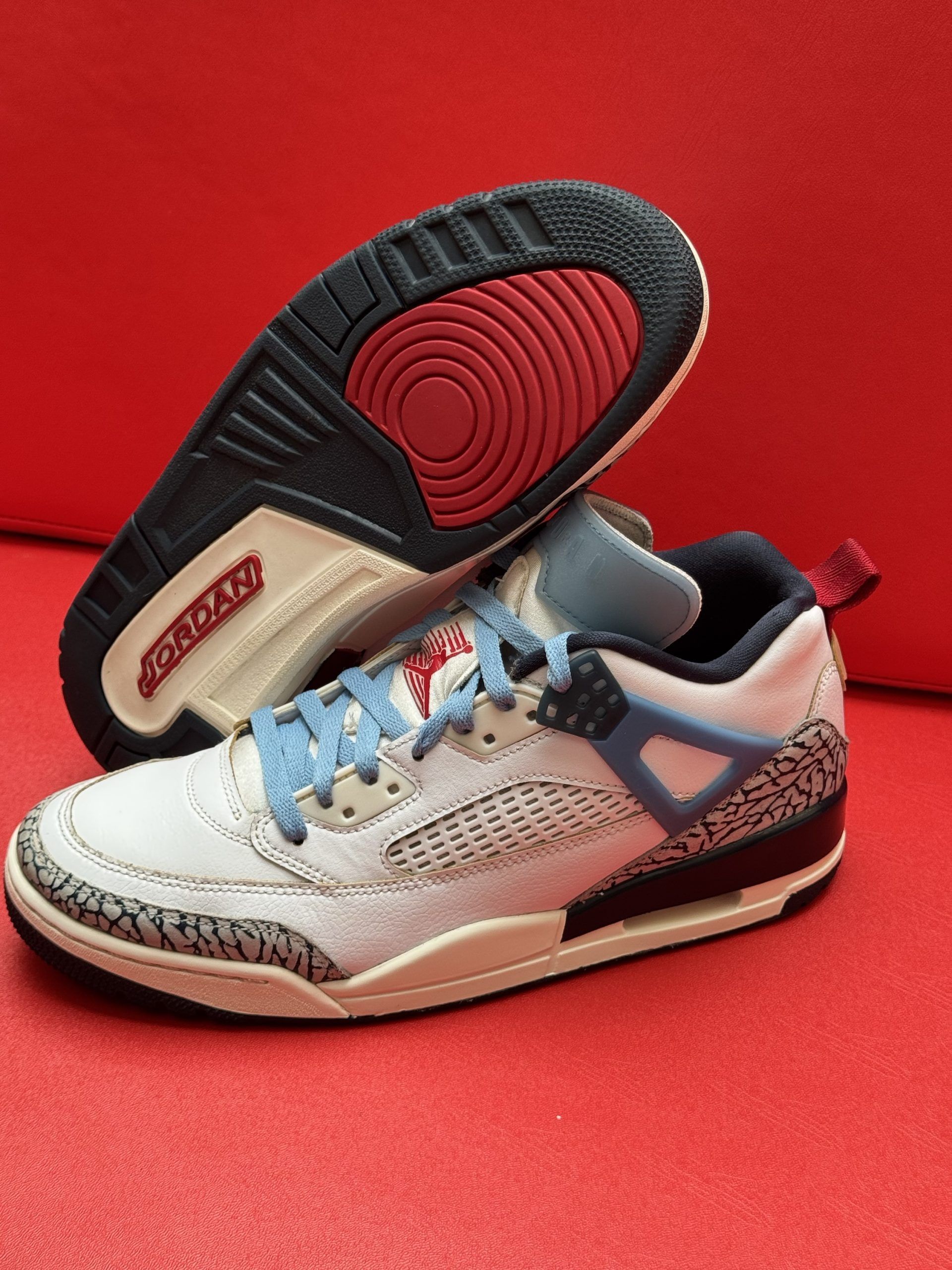 White and blue Air Jordan 3 sneakers with elephant print detailing on a red surface.