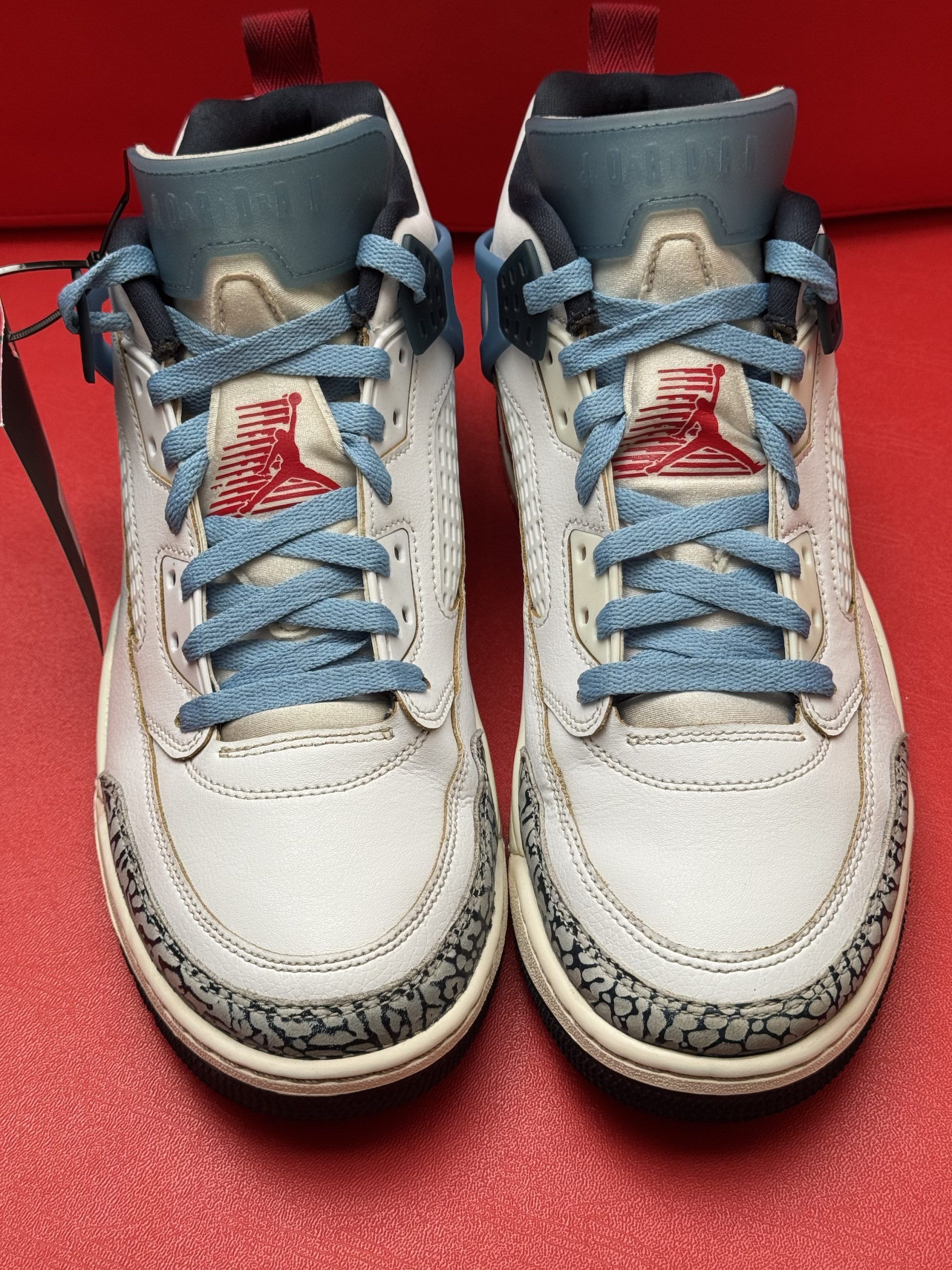 White and blue Air Jordan 3 sneakers with elephant print detailing on a red surface.