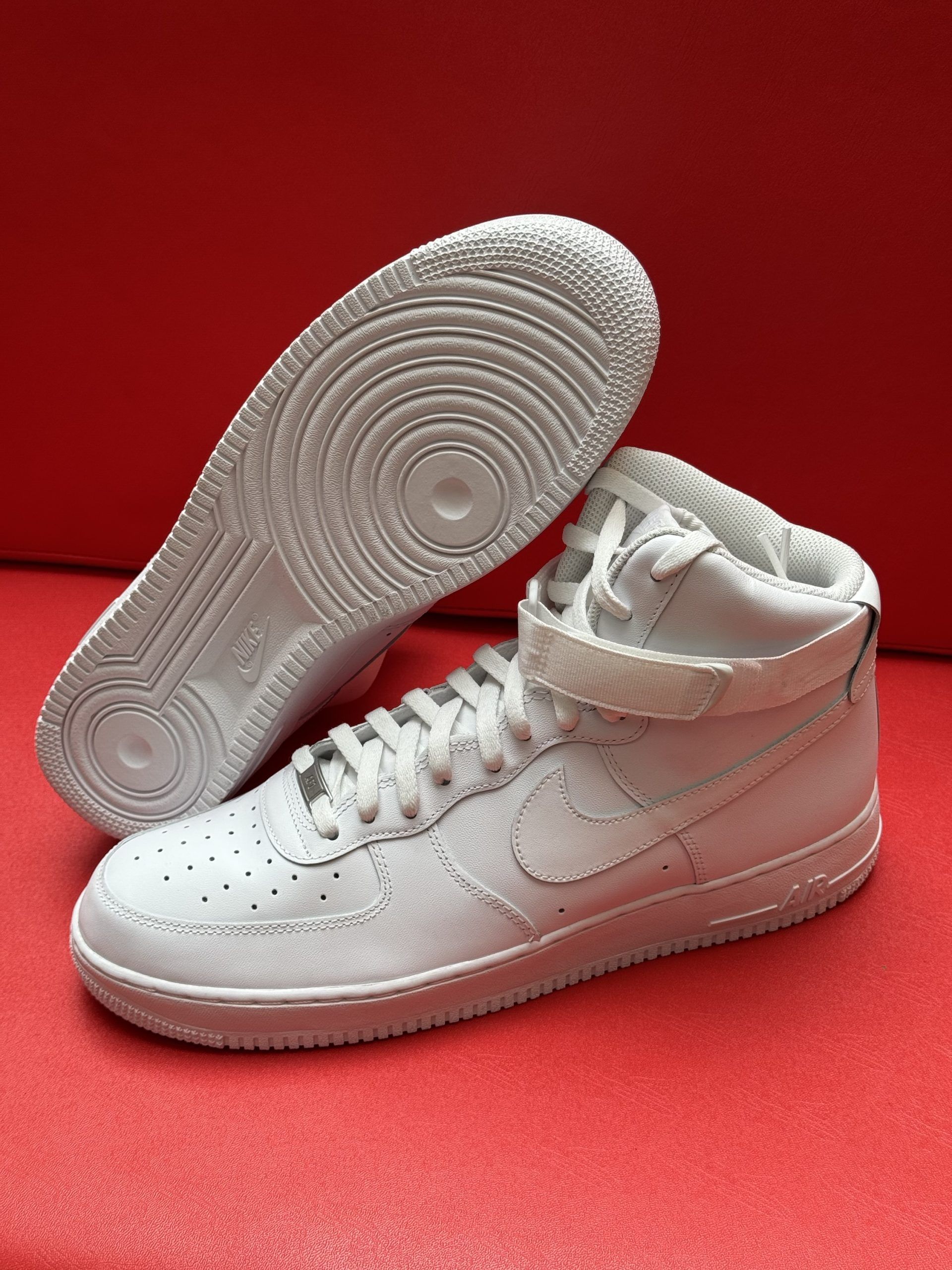 White Nike Air Force 1 high-top sneaker with visible sole on a red background.