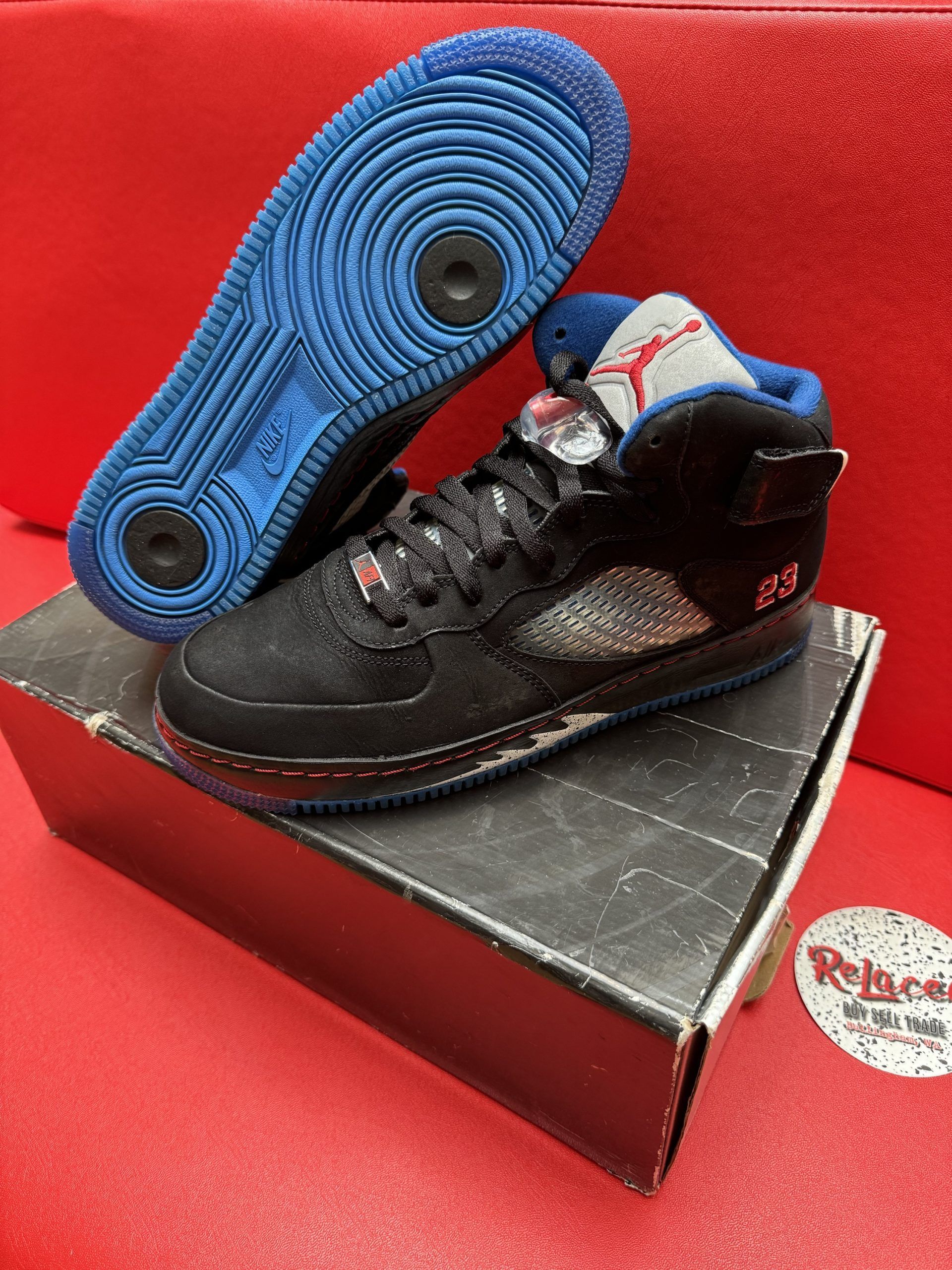 Black and blue Air Jordan 5 hybrid sneakers on a box, red background.