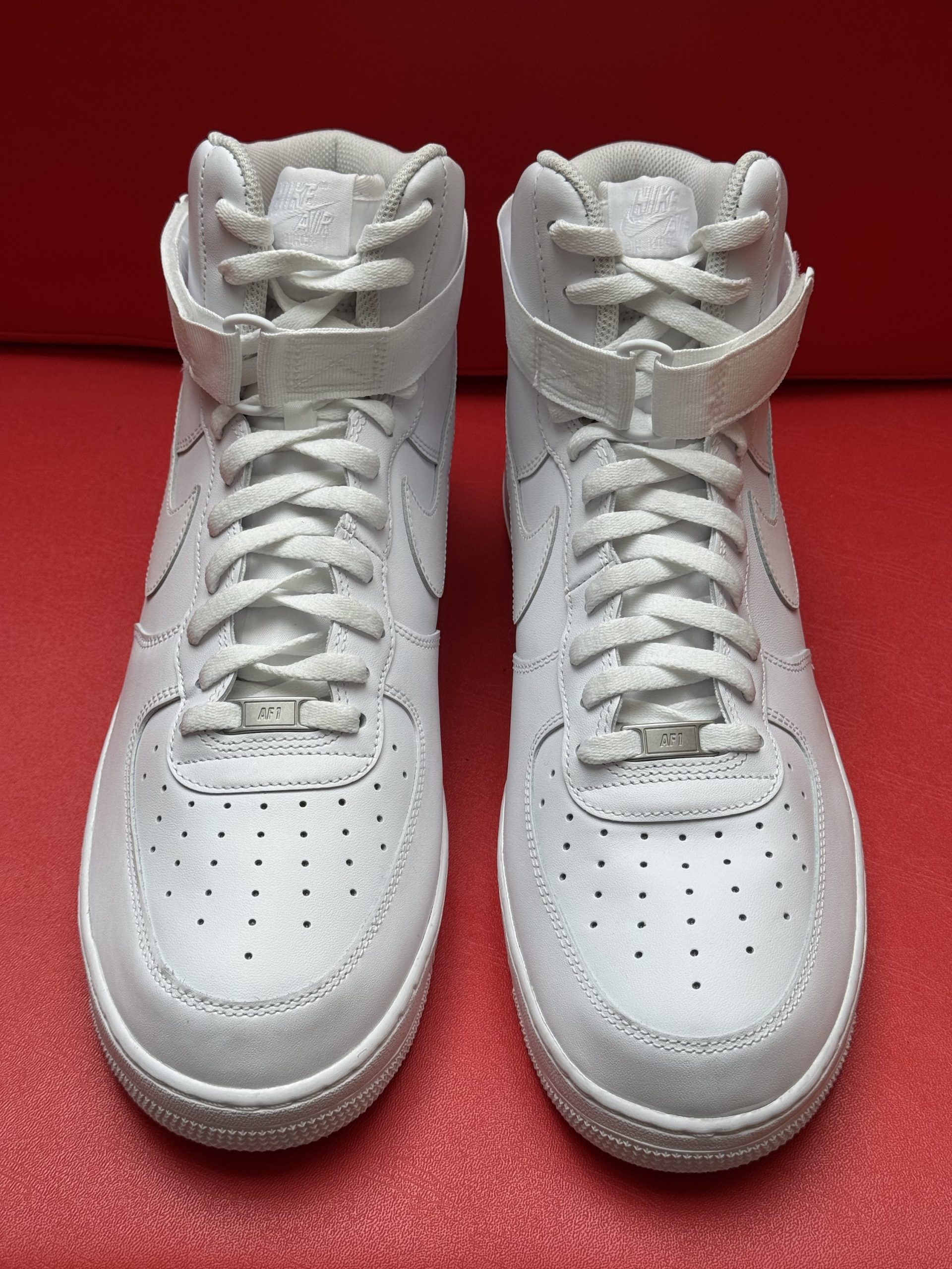 White Nike Air Force 1 high-top sneaker with visible sole on a red background.