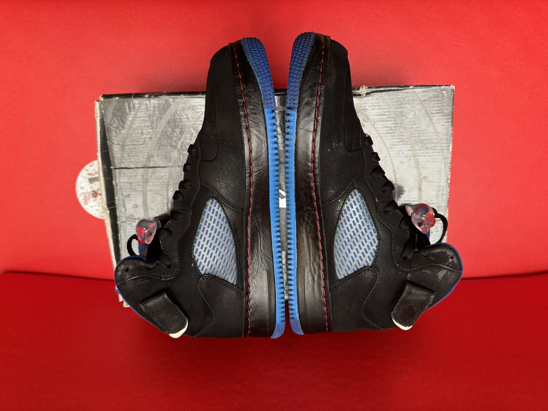 Black and blue Air Jordan 5 hybrid sneakers on a box, red background.