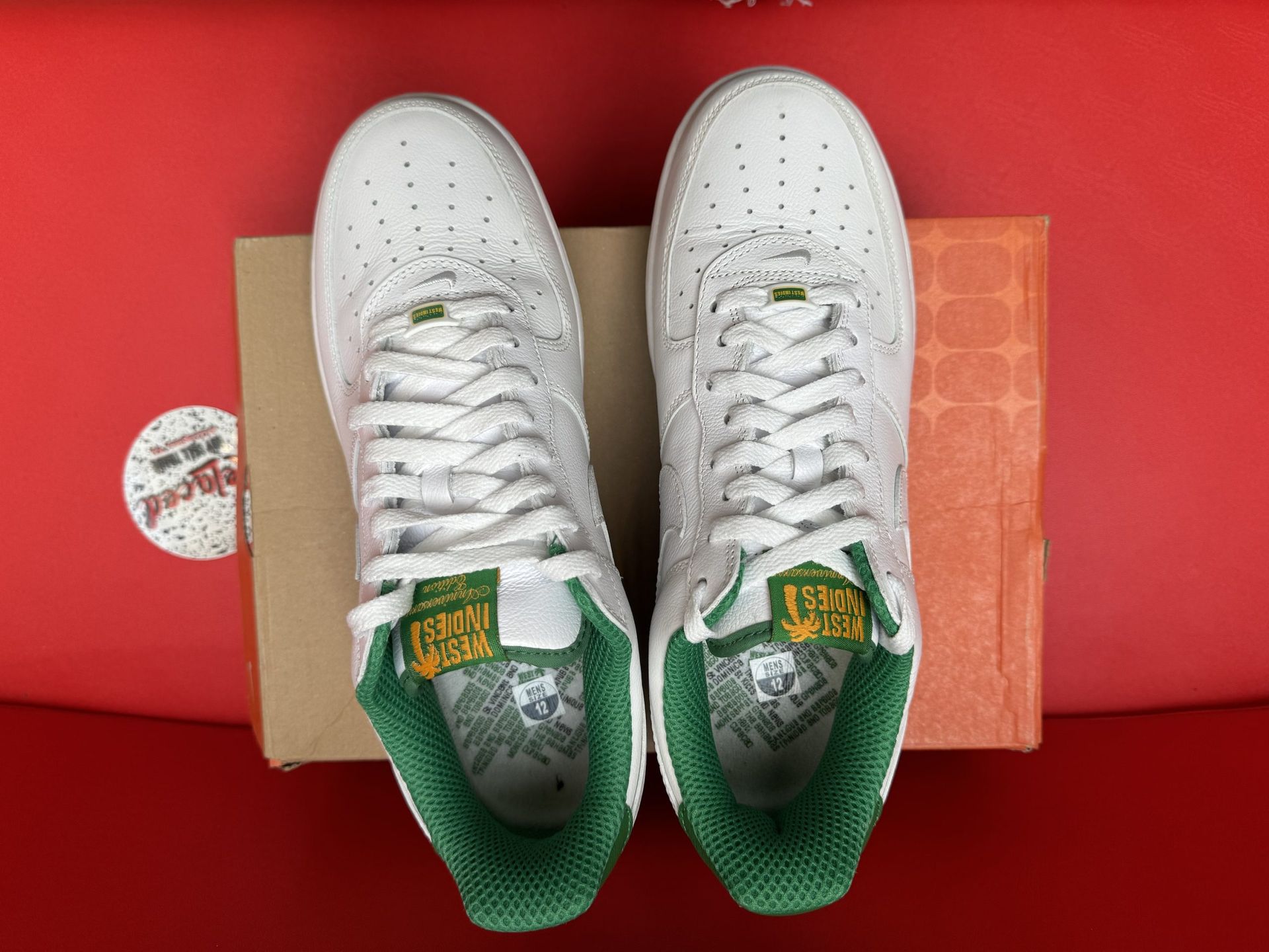 White Nike Air Force 1 sneaker with green accents, box, and sole on red surface.
