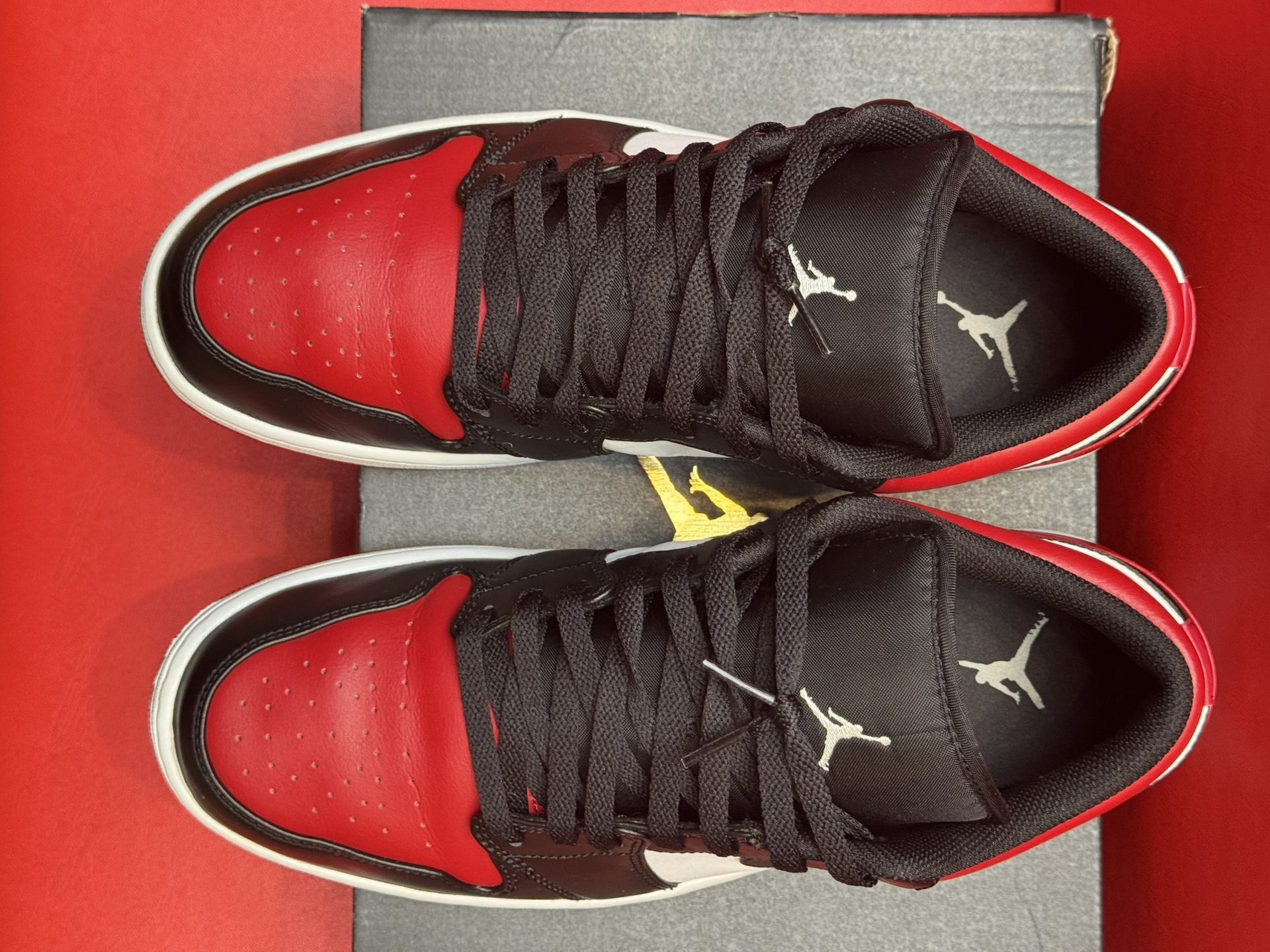 Red, black, and white Air Jordan 1 Low sneakers on a black shoebox, against a red background.