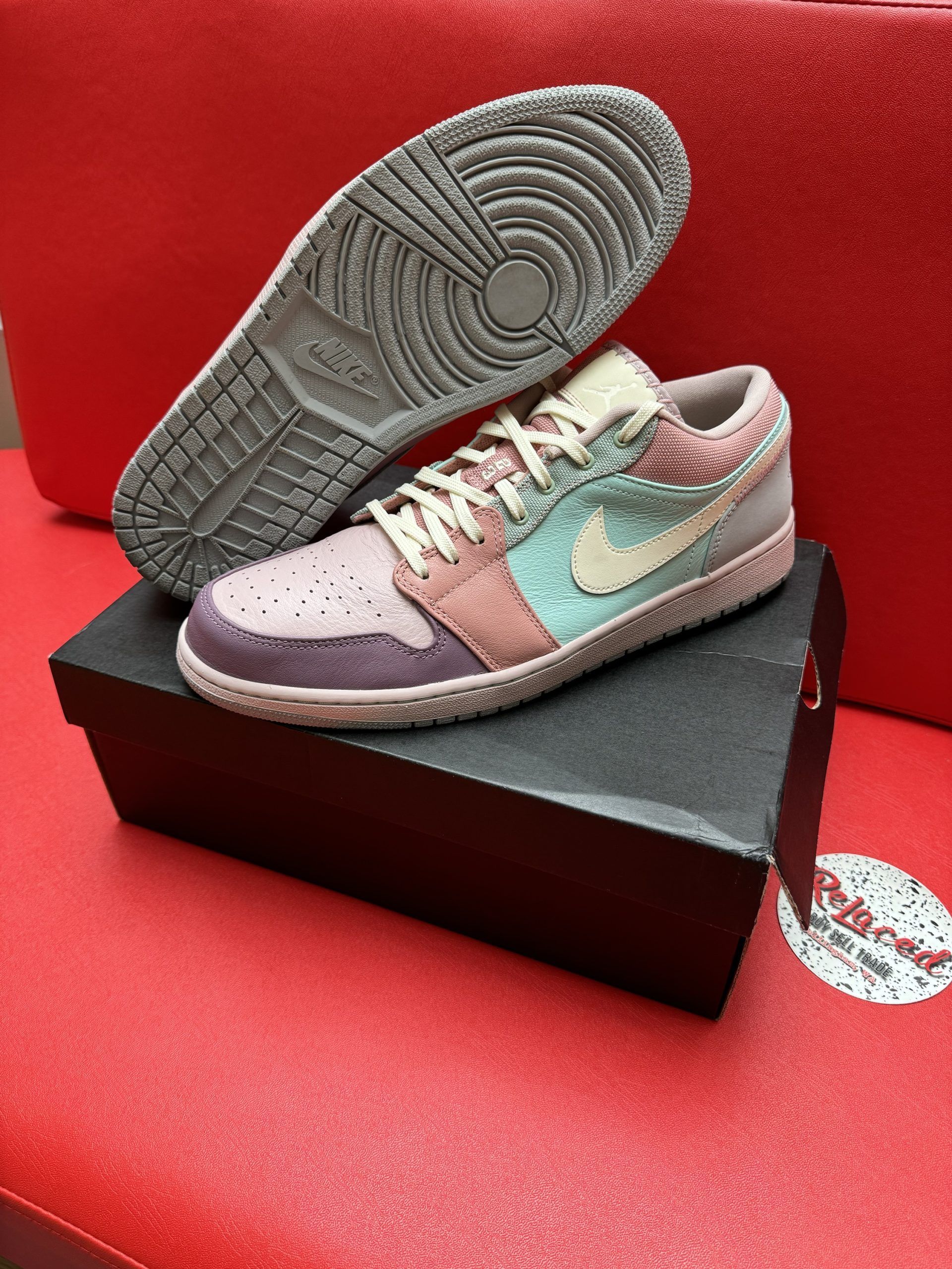 Colorful Air Jordan 1 Low sneaker on a box, with the sole visible. Red background.