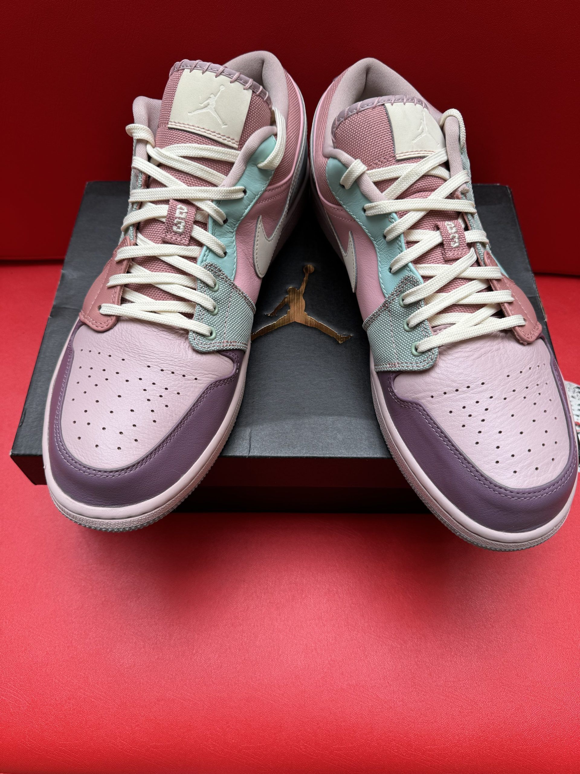 Colorful Air Jordan 1 Low sneaker on a box, with the sole visible. Red background.