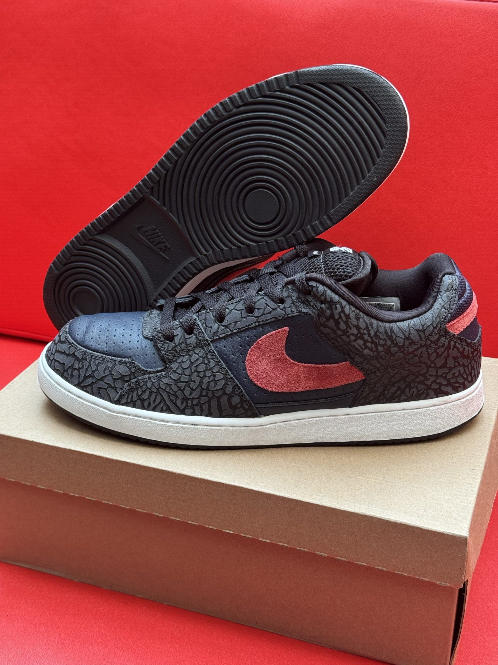 Nike Court Vision low-top sneakers in navy and red, set on a cardboard box against a red background.