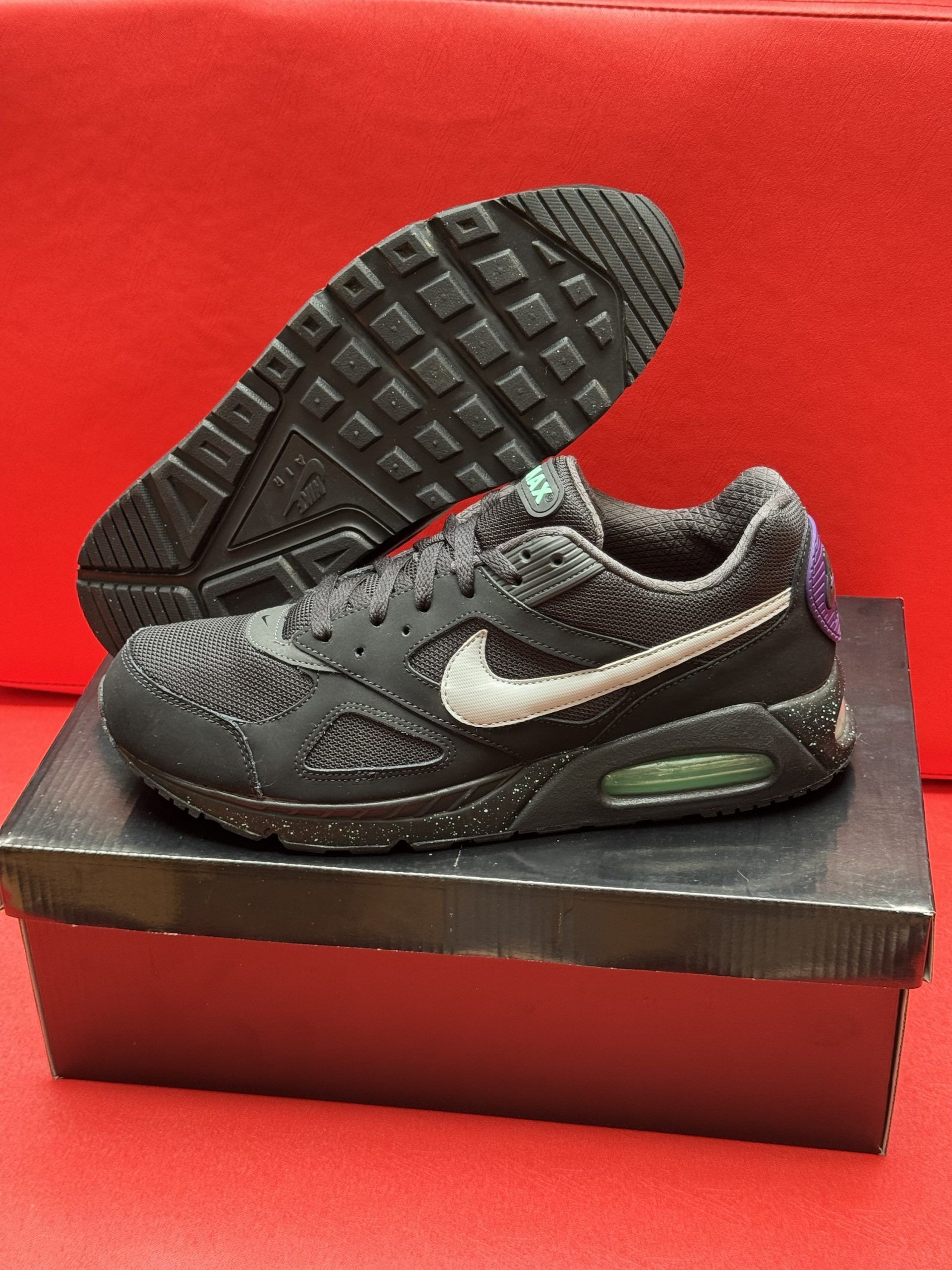 Black Nike Air Max sneakers on a black box, one shoe's sole visible, set against a red background.