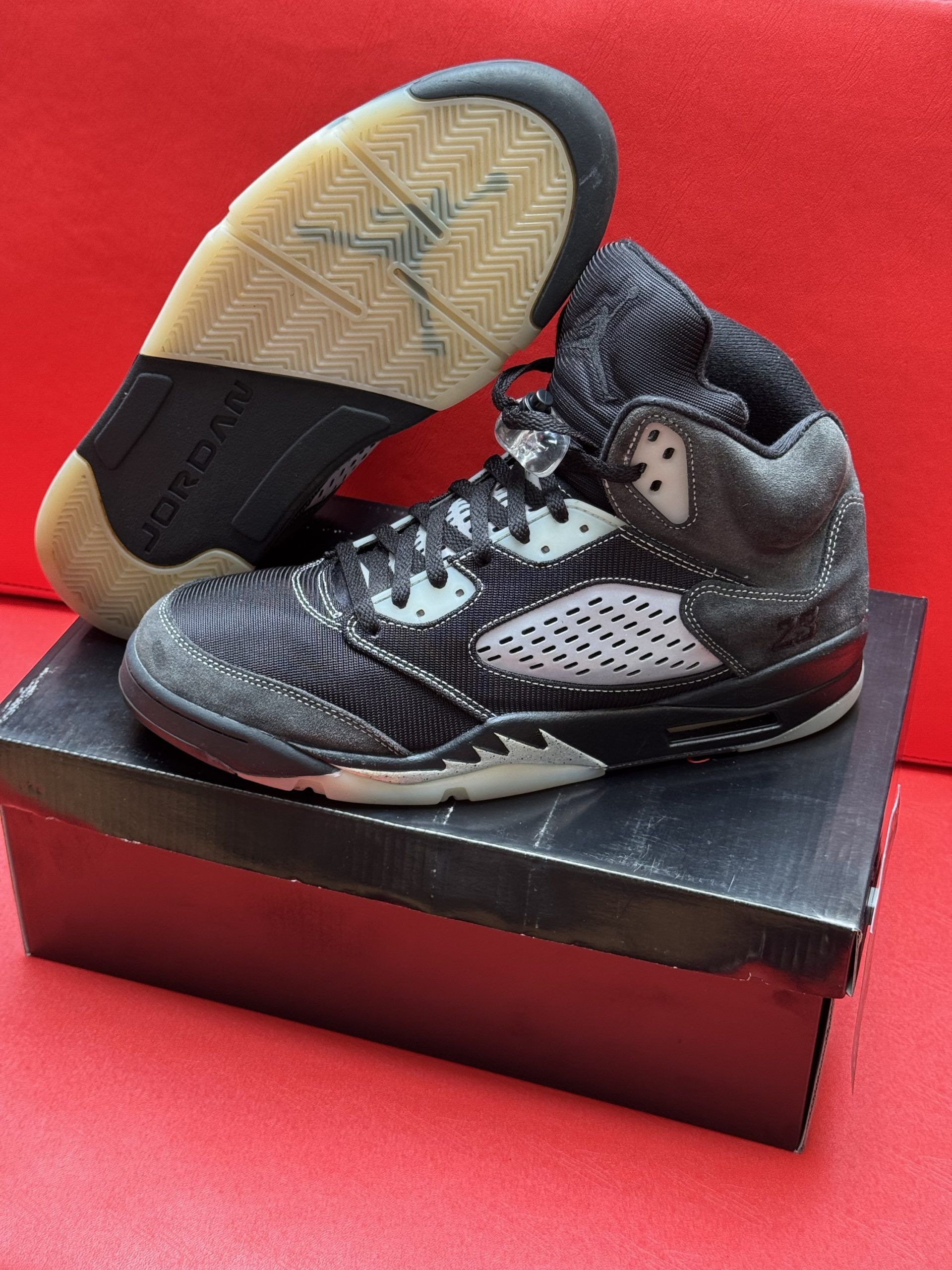 Black and gray Air Jordan 5 sneakers on a black shoebox, sole visible.