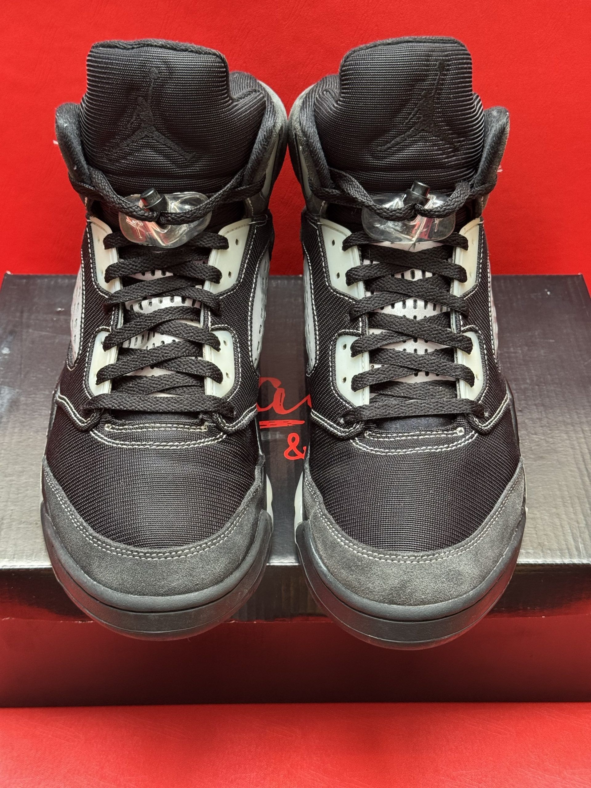 Black and gray Air Jordan 5 sneakers on a black shoebox, sole visible.