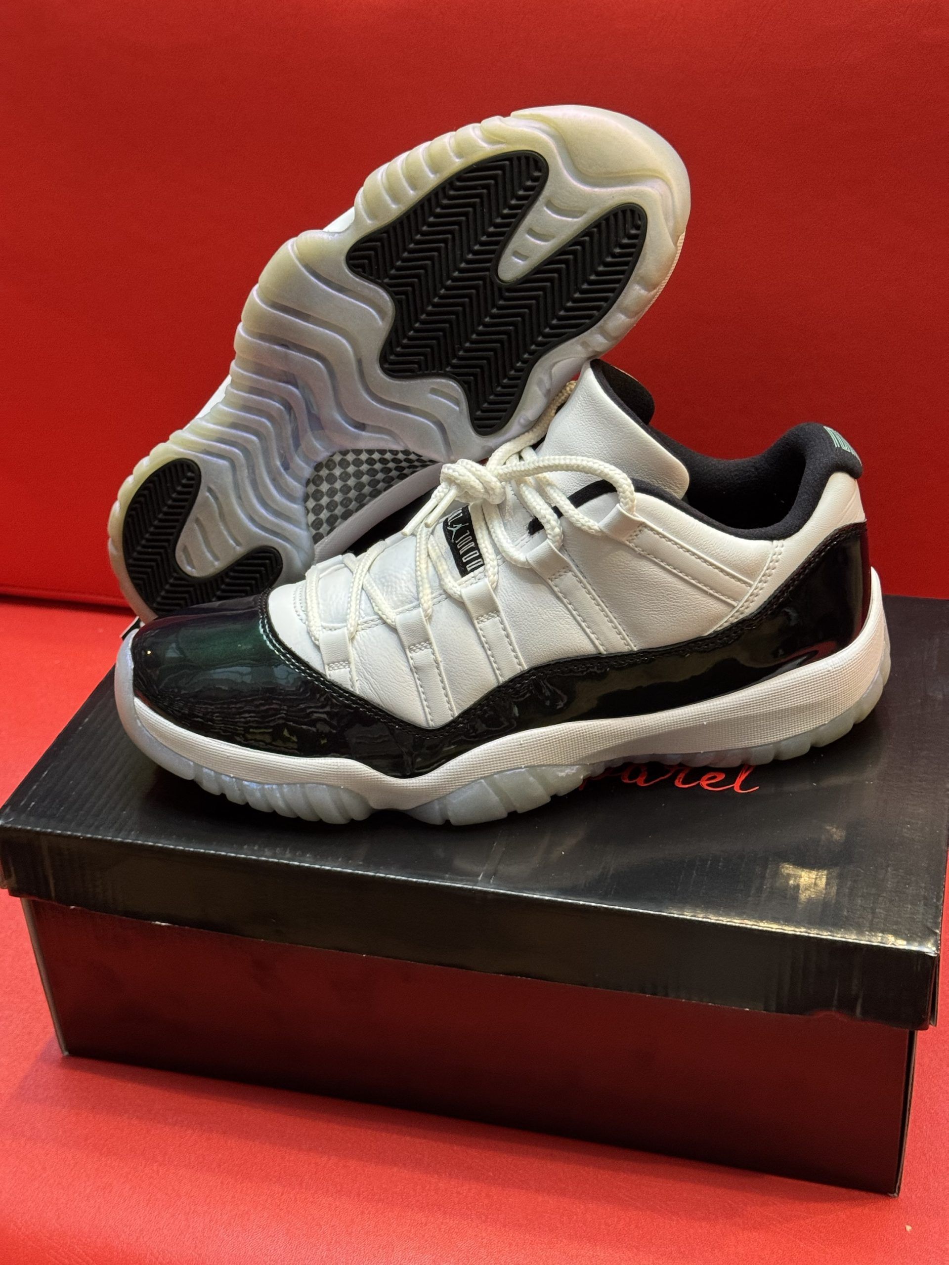 White and black Air Jordan 11 low-top sneakers on a shoebox, set against a red background.