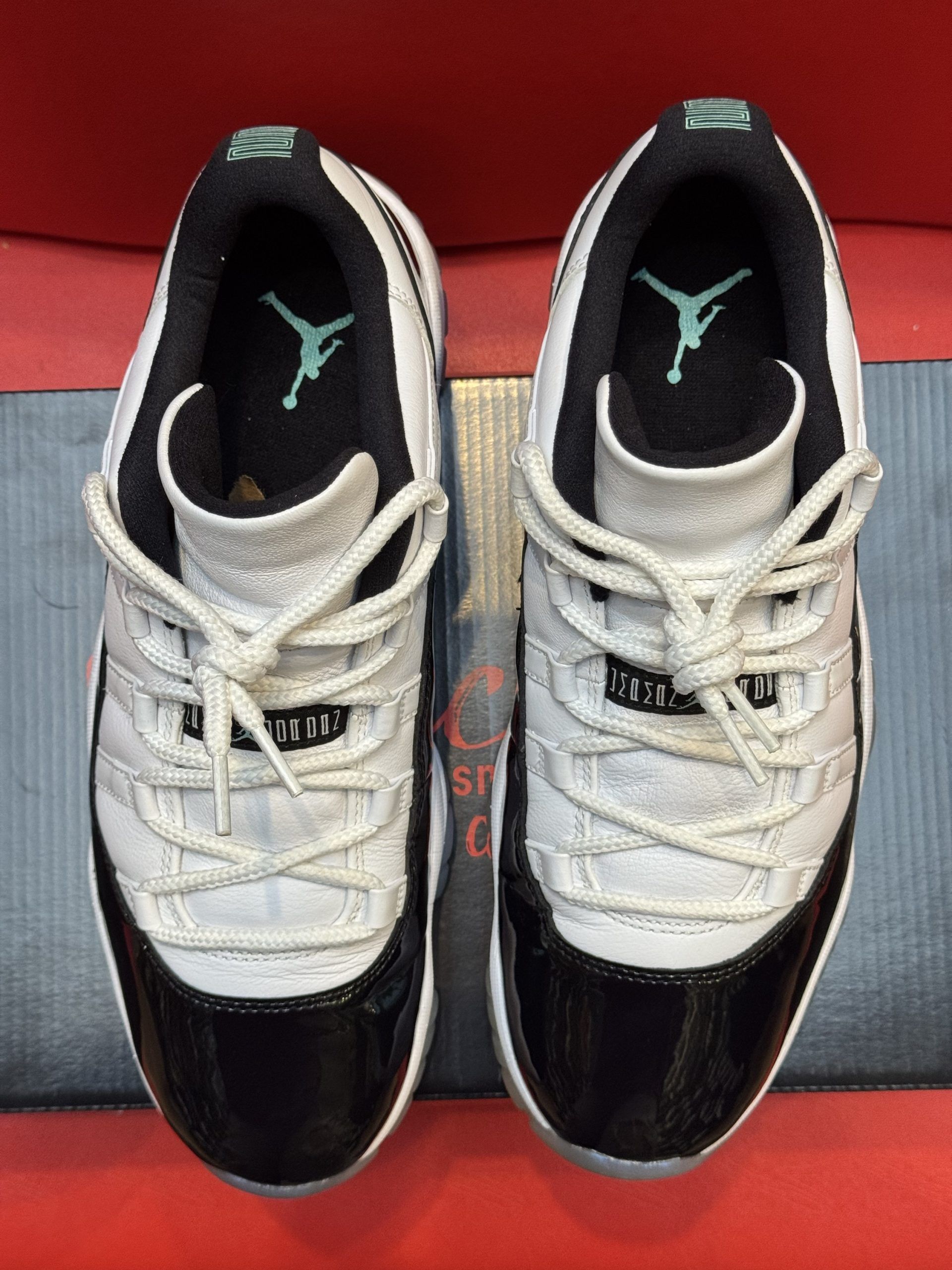White and black Air Jordan 11 low-top sneakers on a shoebox, set against a red background.