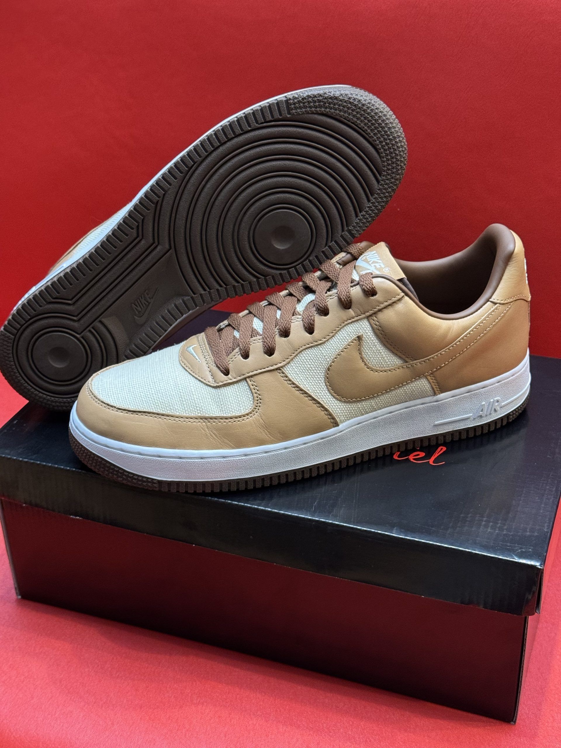 Brown and tan Nike Air Force 1 sneakers on a black box, red background.
