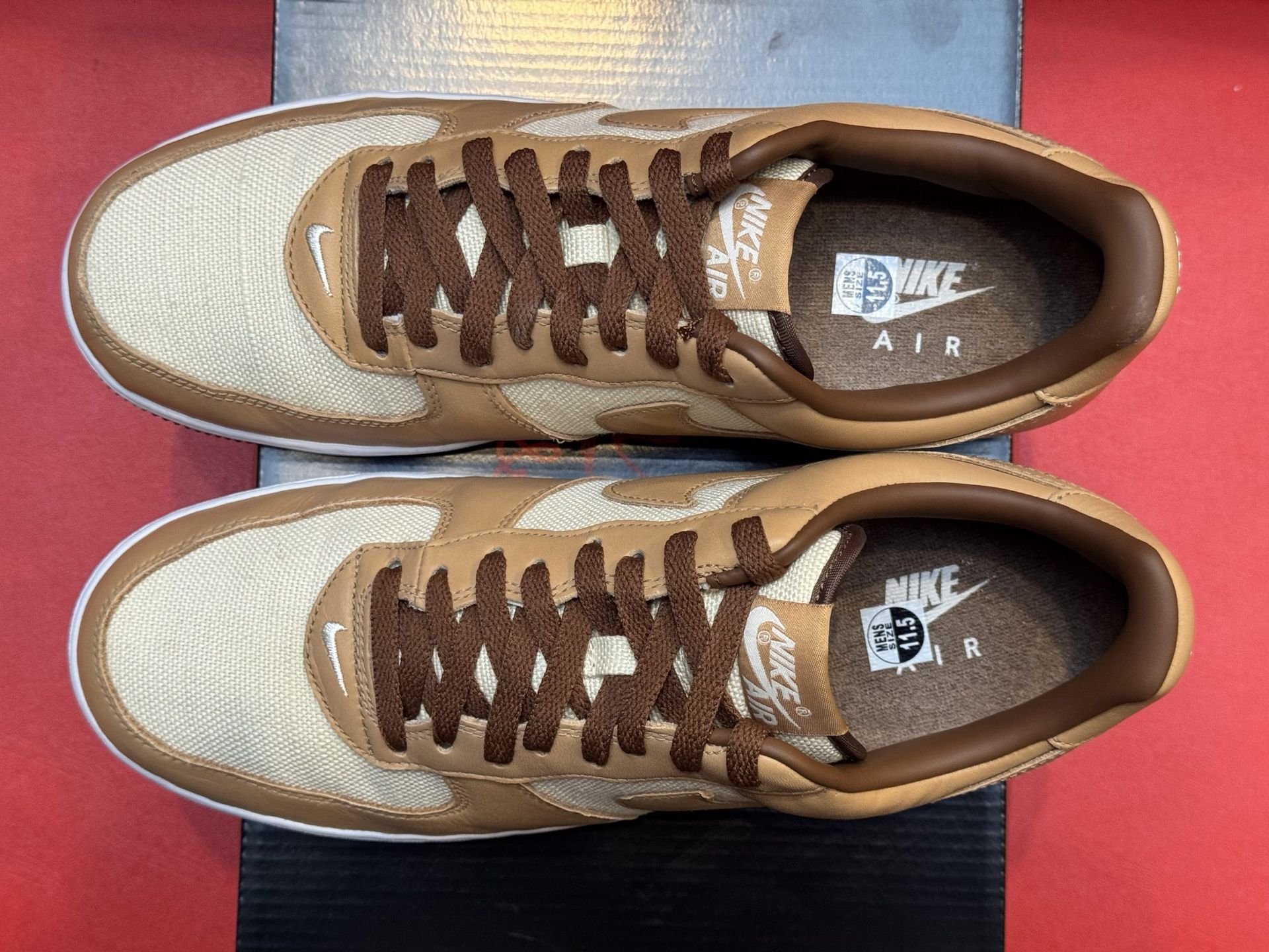 Brown and tan Nike Air Force 1 sneakers on a black box, red background.