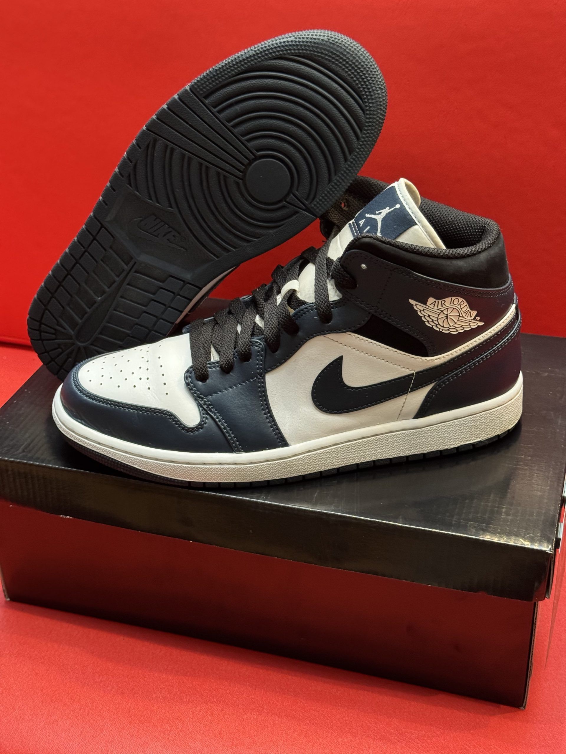 Air Jordan 1 Mid sneaker in blue, white, and black, with the sole visible. The sneaker sits on a shoe box.