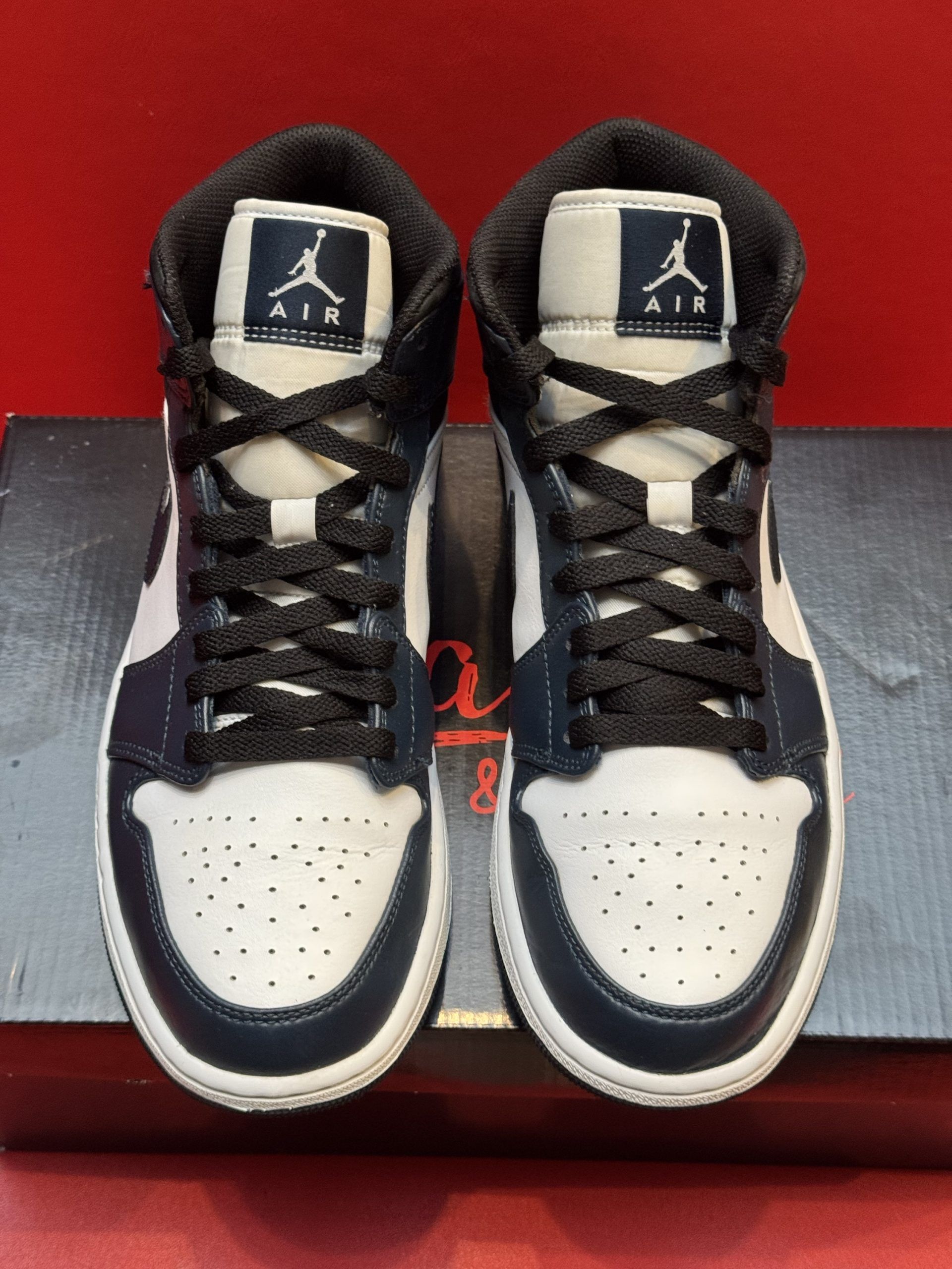 Air Jordan 1 Mid sneaker in blue, white, and black, with the sole visible. The sneaker sits on a shoe box.