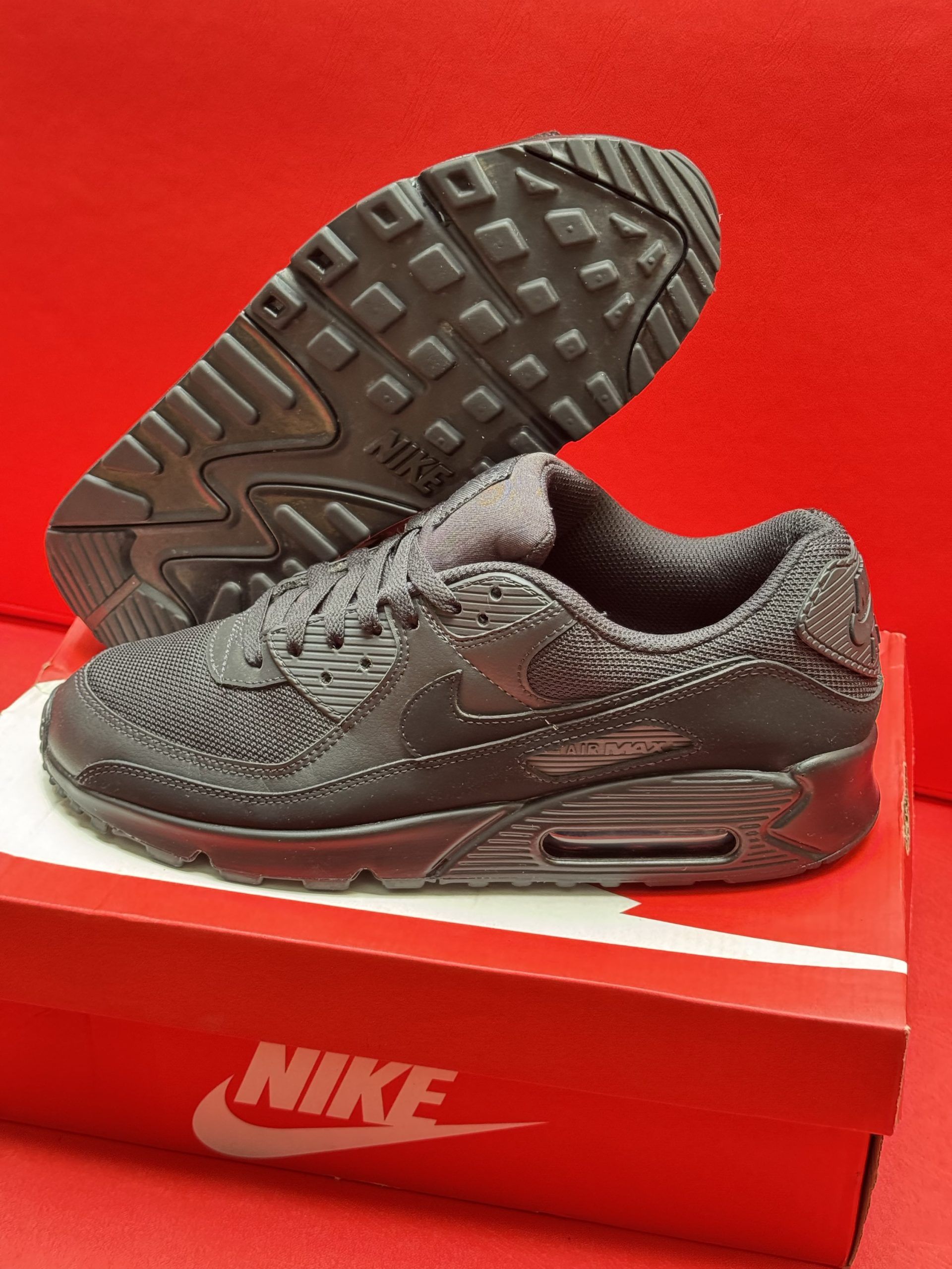 Black Nike Air Max 90 sneakers on a red Nike box, against a red background.
