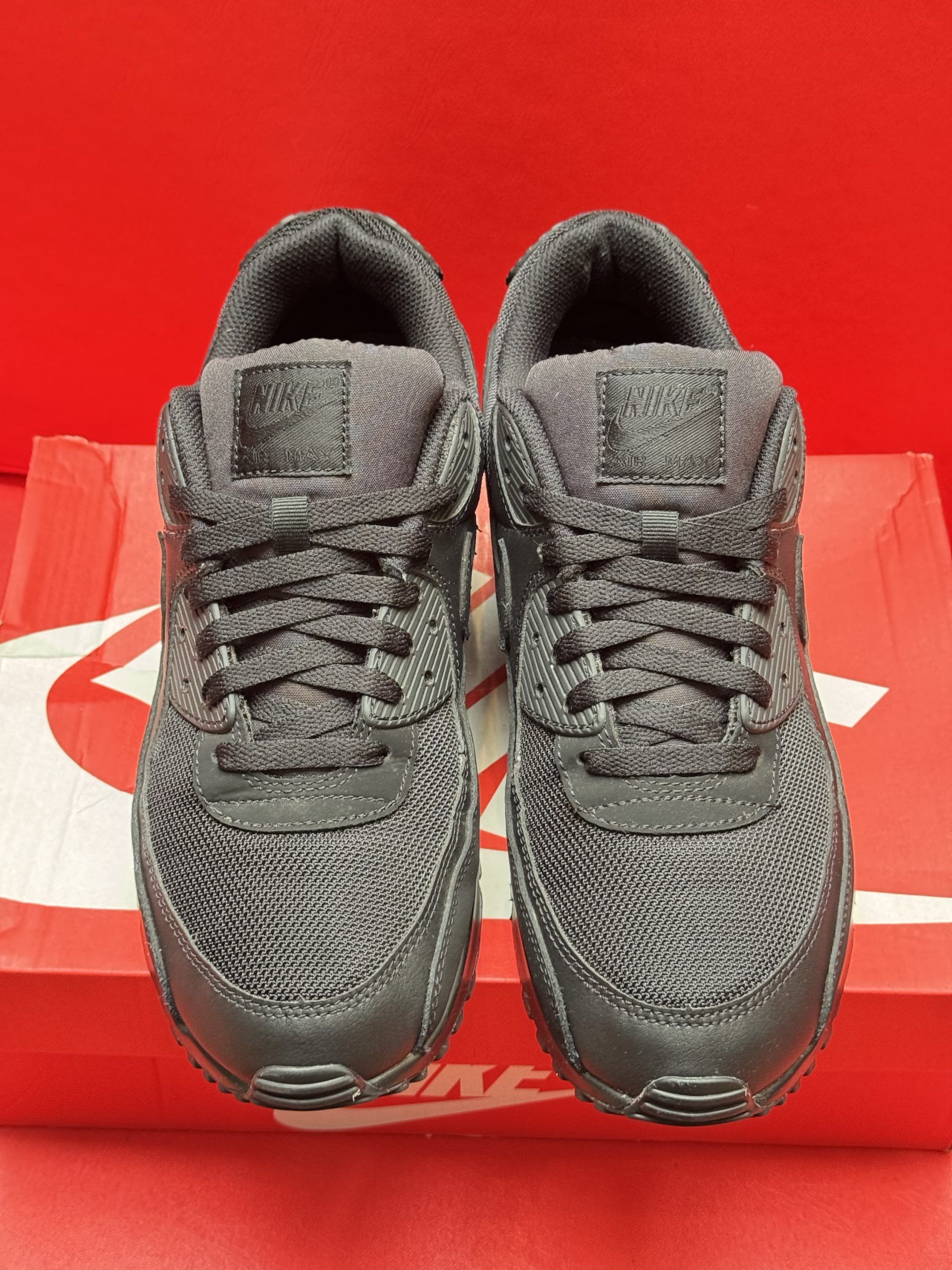 Black Nike Air Max 90 sneakers on a red Nike box, against a red background.