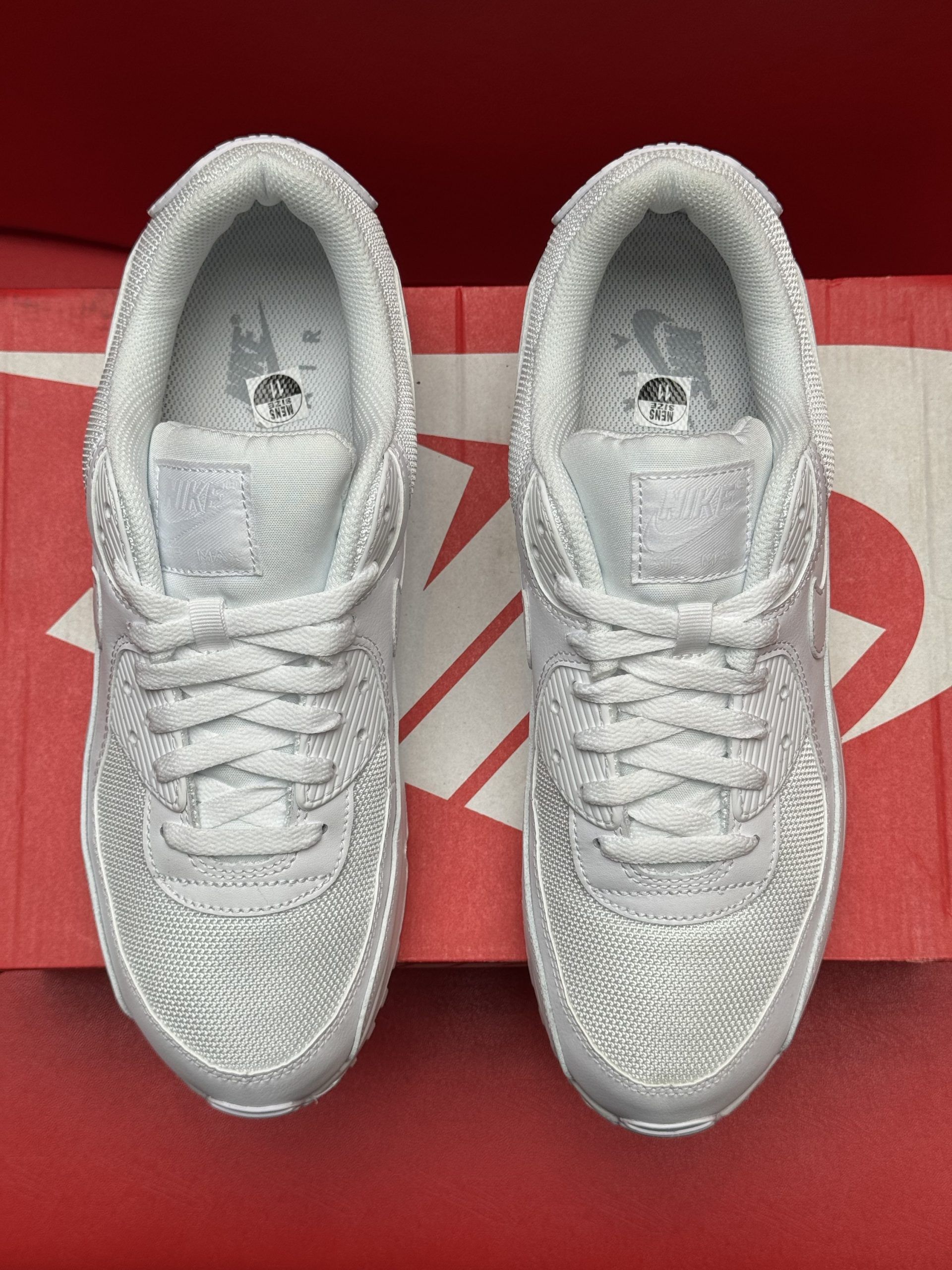 White Nike Air Max 90 sneakers on a red Nike box, with the sole visible.