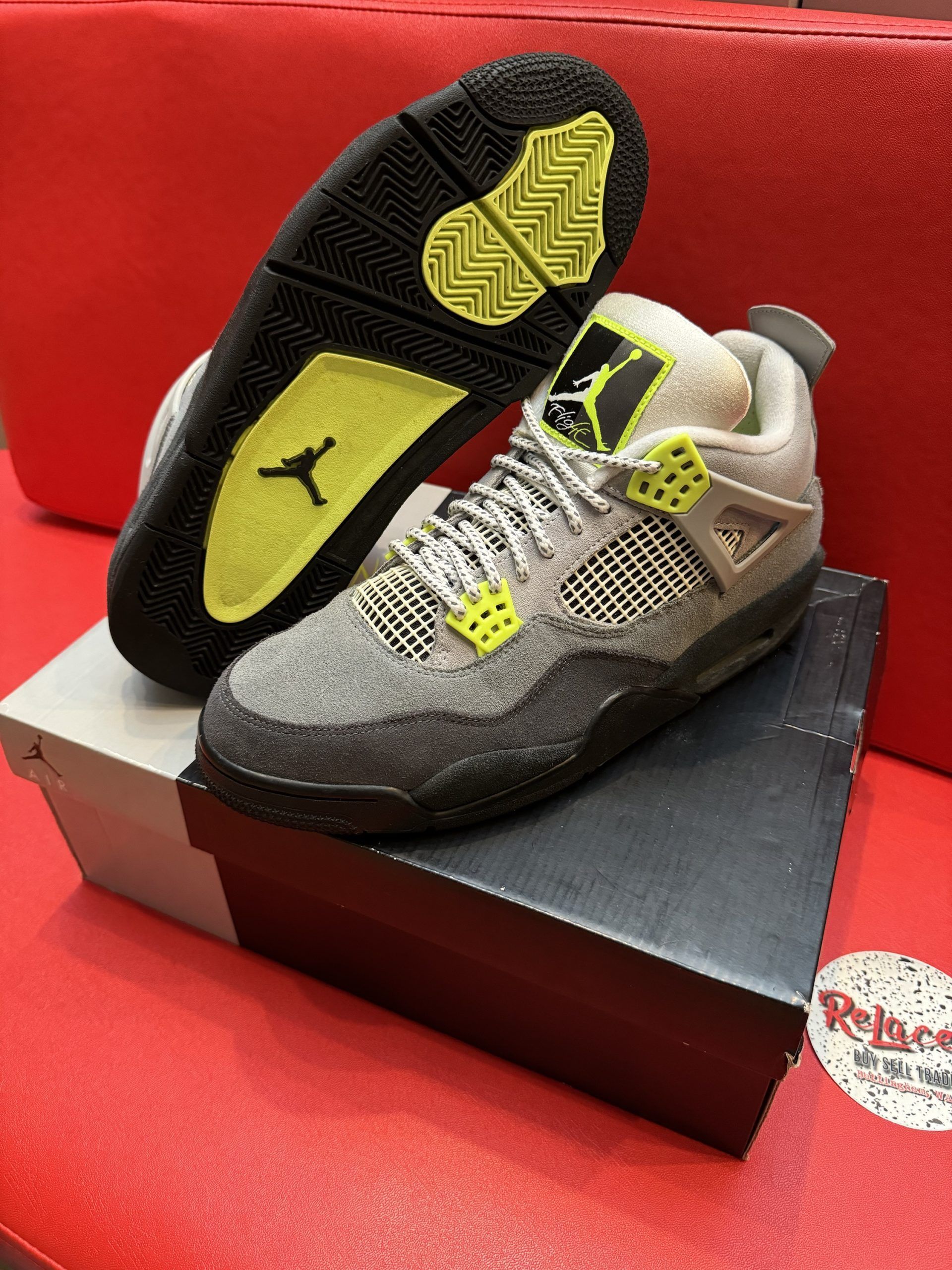 Gray and black Air Jordan 4 sneakers with yellow accents, displayed on a shoebox.