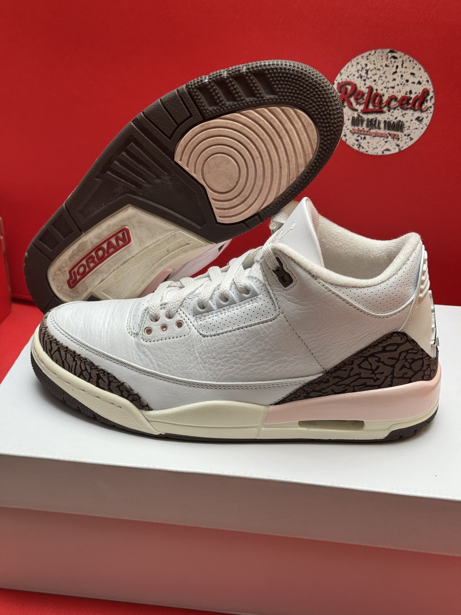 Air Jordan 3 sneakers in white and brown, on a white box with a red backdrop.
