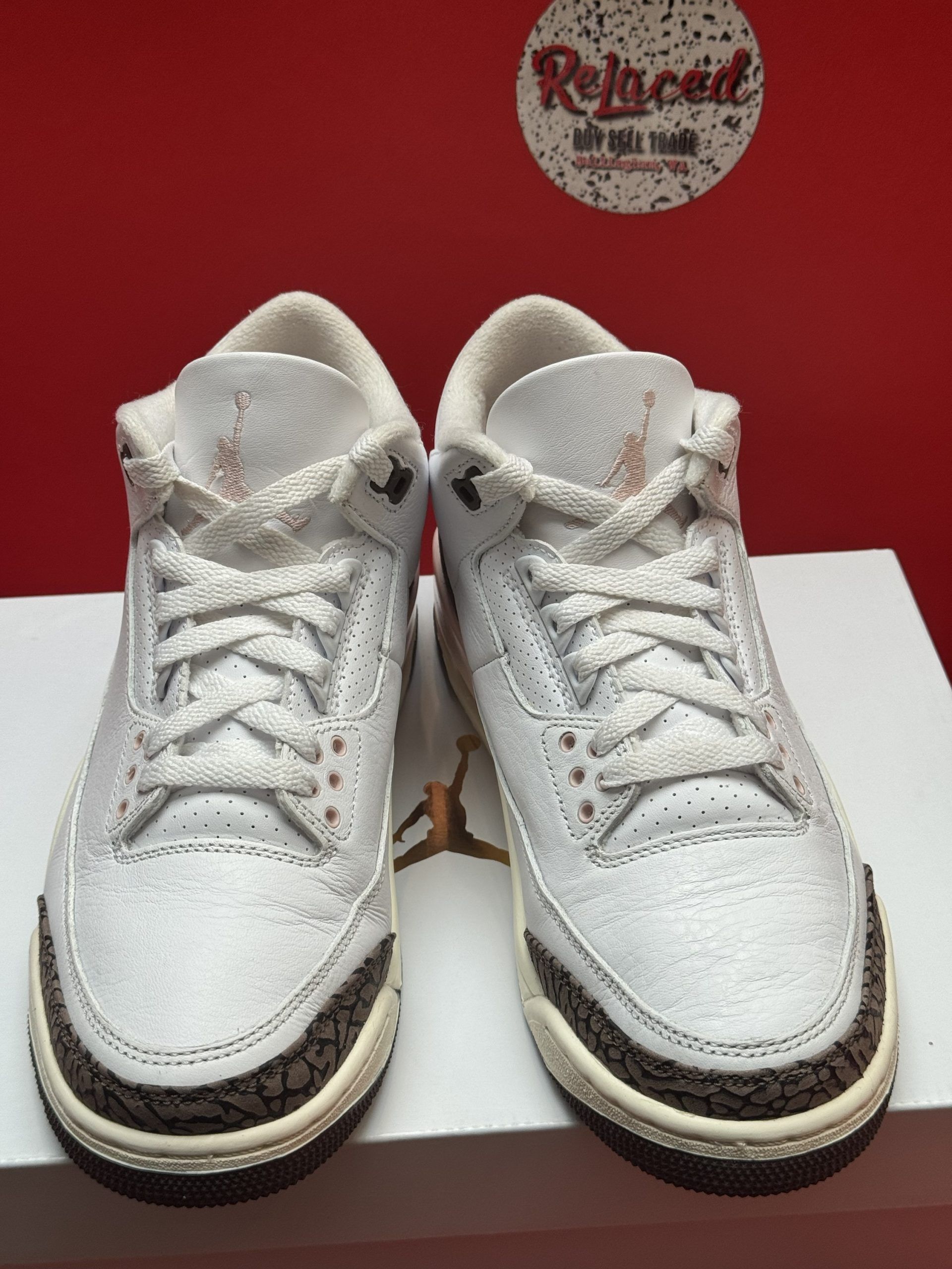 Air Jordan 3 sneakers in white and brown, on a white box with a red backdrop.