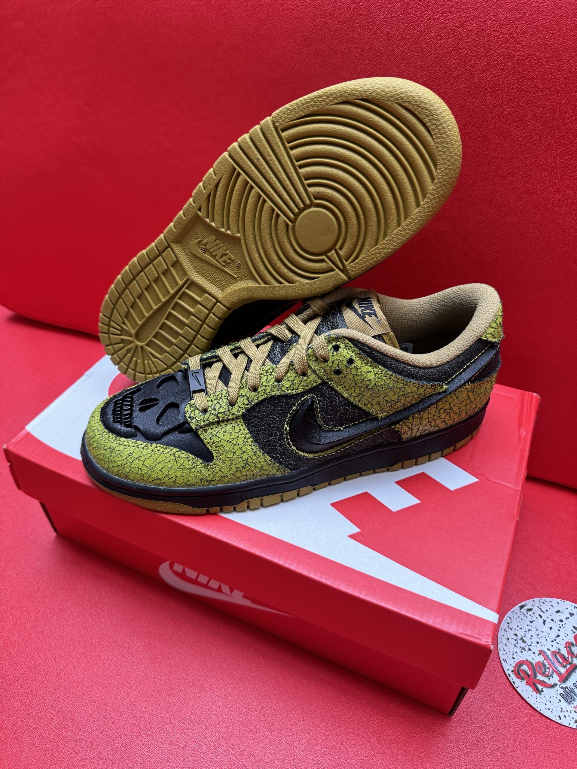 Nike Dunk Low sneakers, green and black, sitting on a red Nike shoe box with a matching sole against a red background.