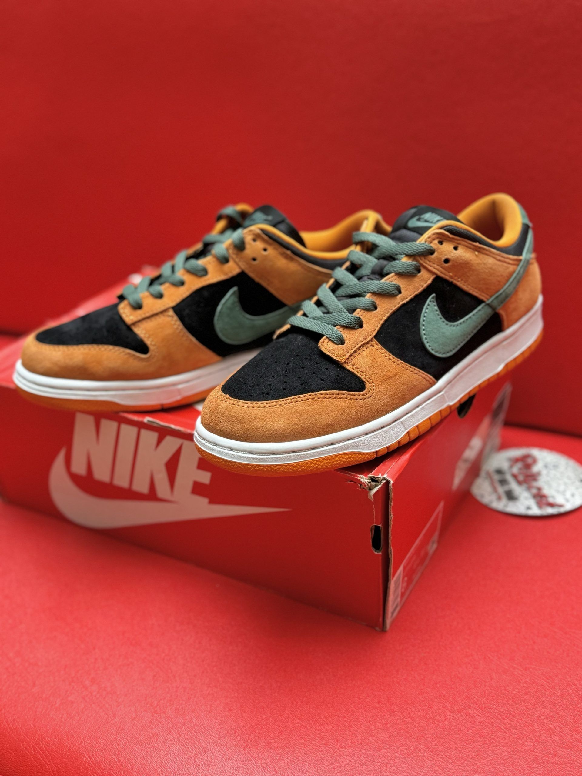 Nike Dunk Low sneakers, brown, black, and teal, on red Nike box. Orange sole visible.