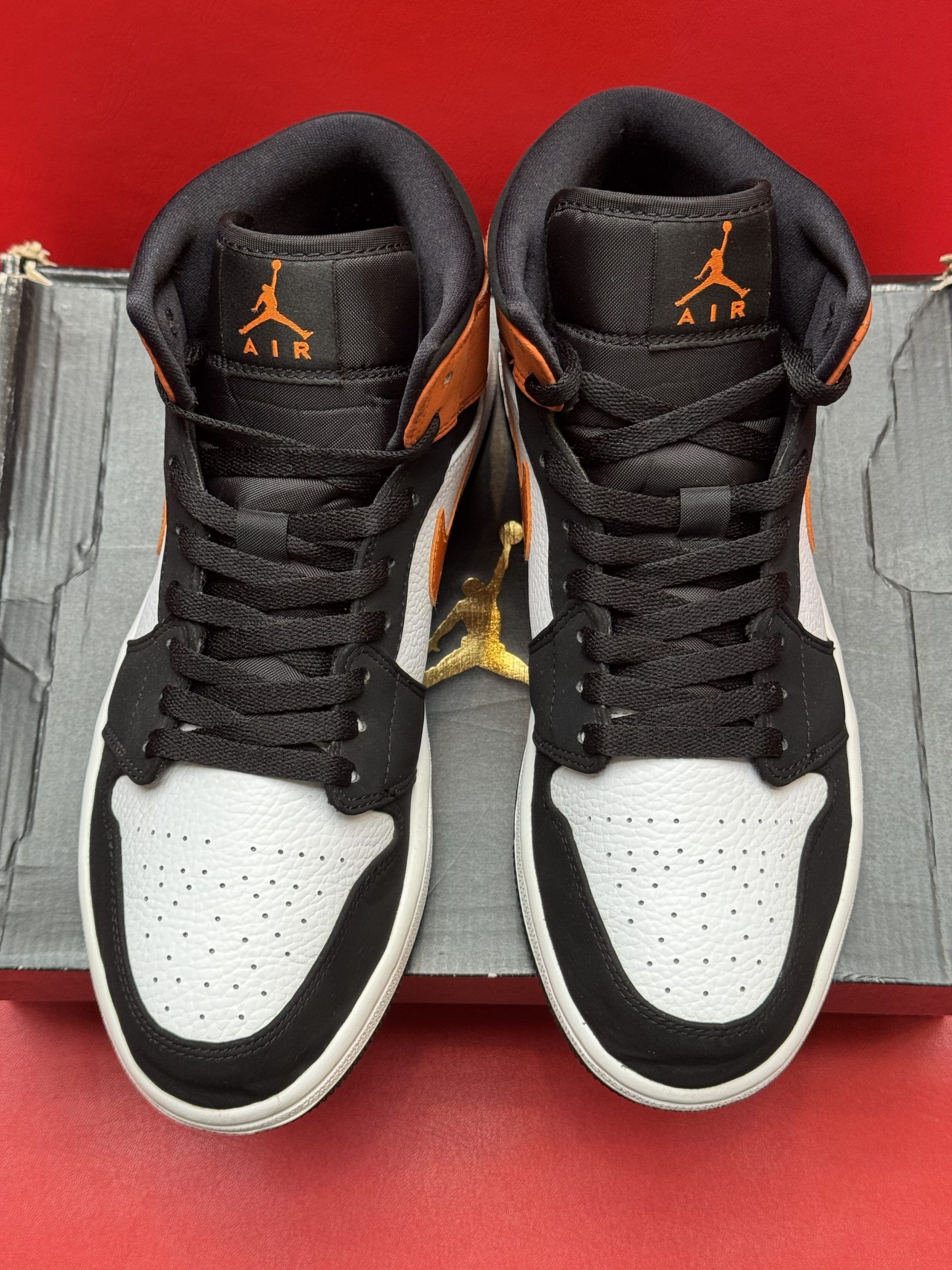 Orange and black Air Jordan sneaker on a black box, with the sole visible.