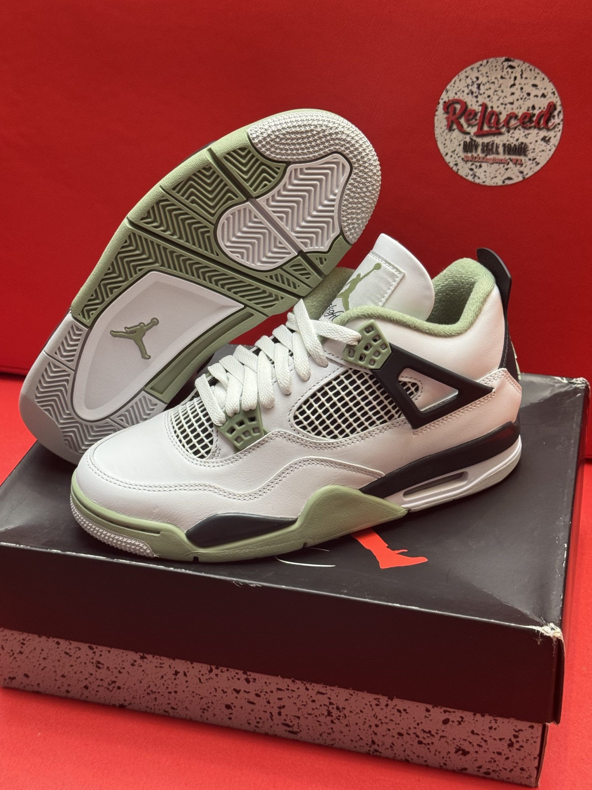White, green, and black Air Jordan 4 sneakers on top of a shoe box with a red background.