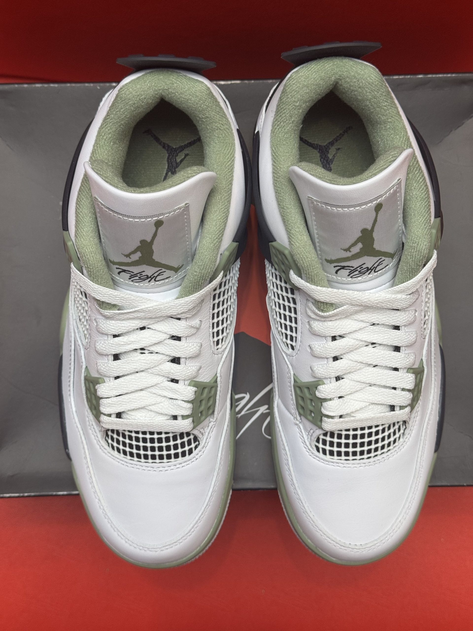 White, green, and black Air Jordan 4 sneakers on top of a shoe box with a red background.