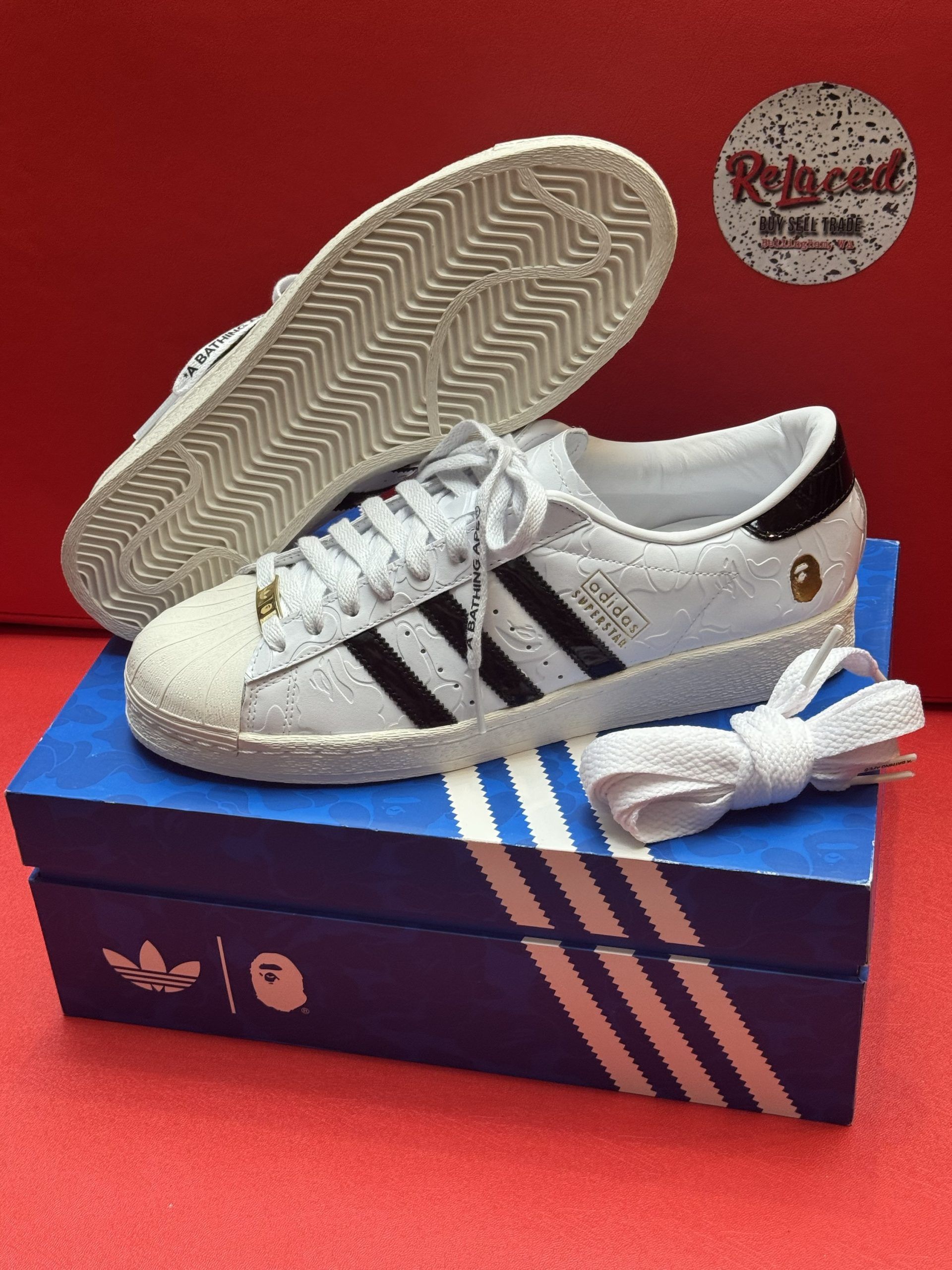 White Adidas Superstar sneakers with black stripes, laces, and a box.
