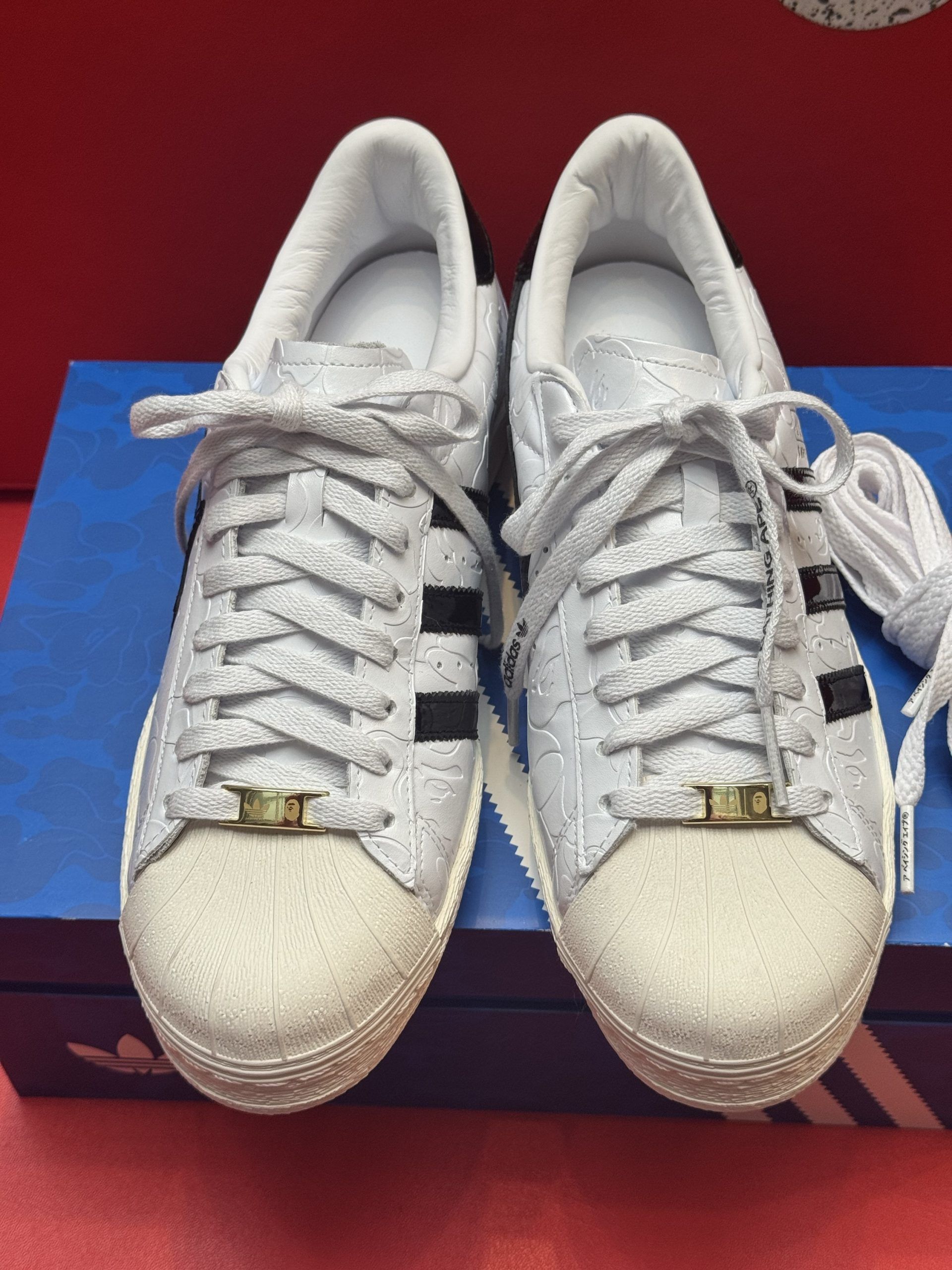 White Adidas Superstar sneakers with black stripes, laces, and a box.