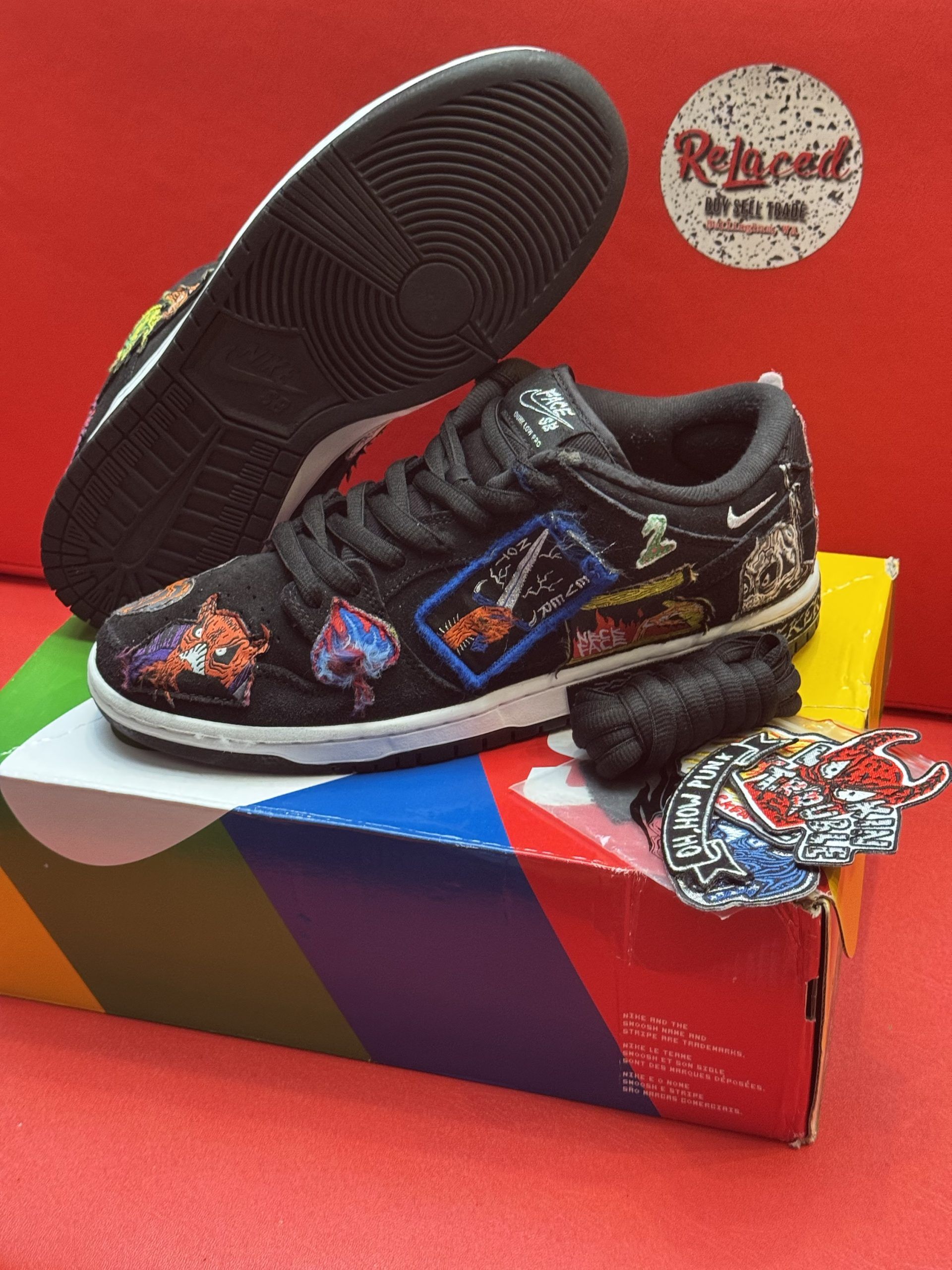 Black and colorful Nike Dunk Low sneakers with unique patches, sitting on a colorful shoebox with accessories.