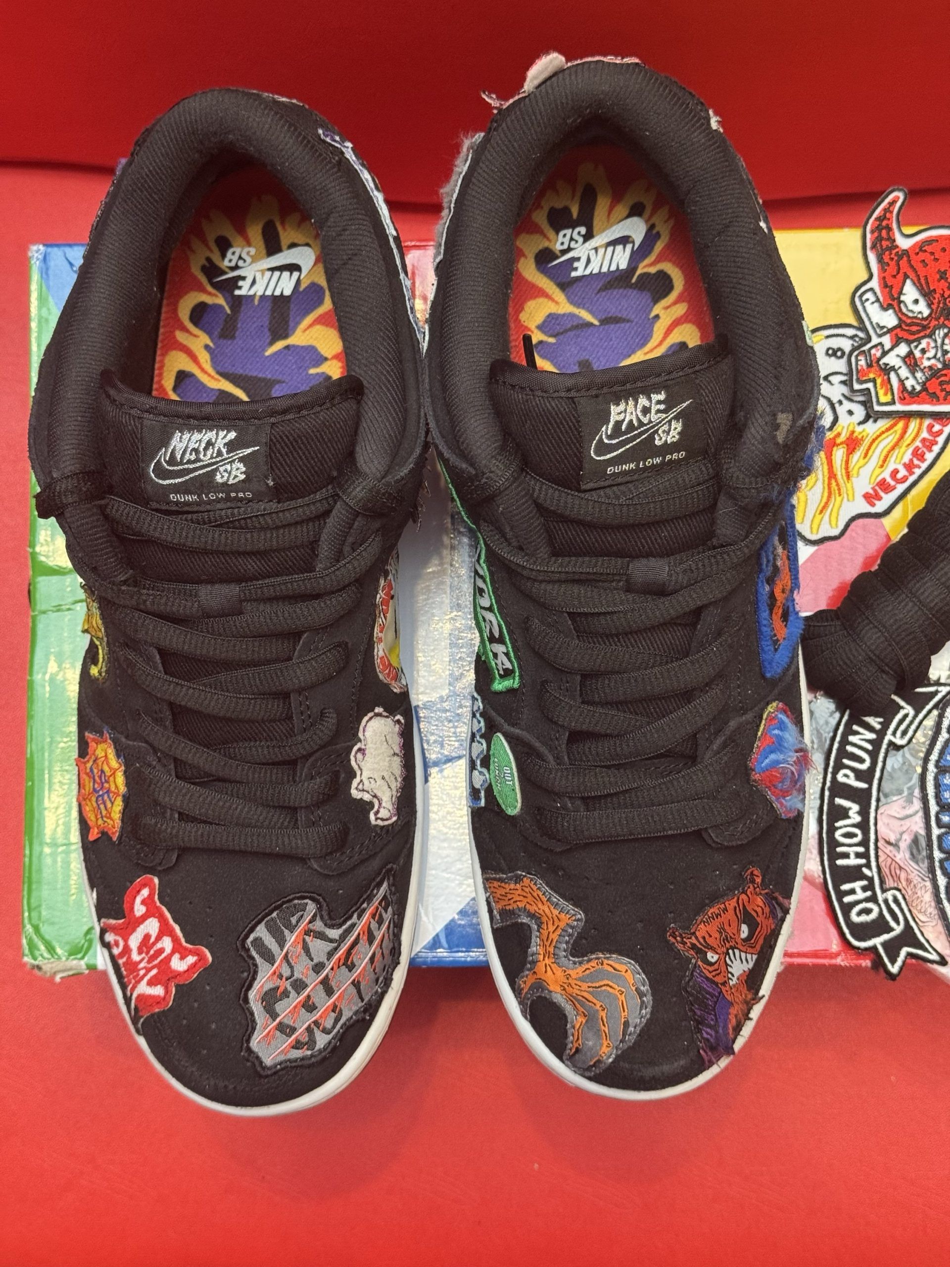 Black and colorful Nike Dunk Low sneakers with unique patches, sitting on a colorful shoebox with accessories.