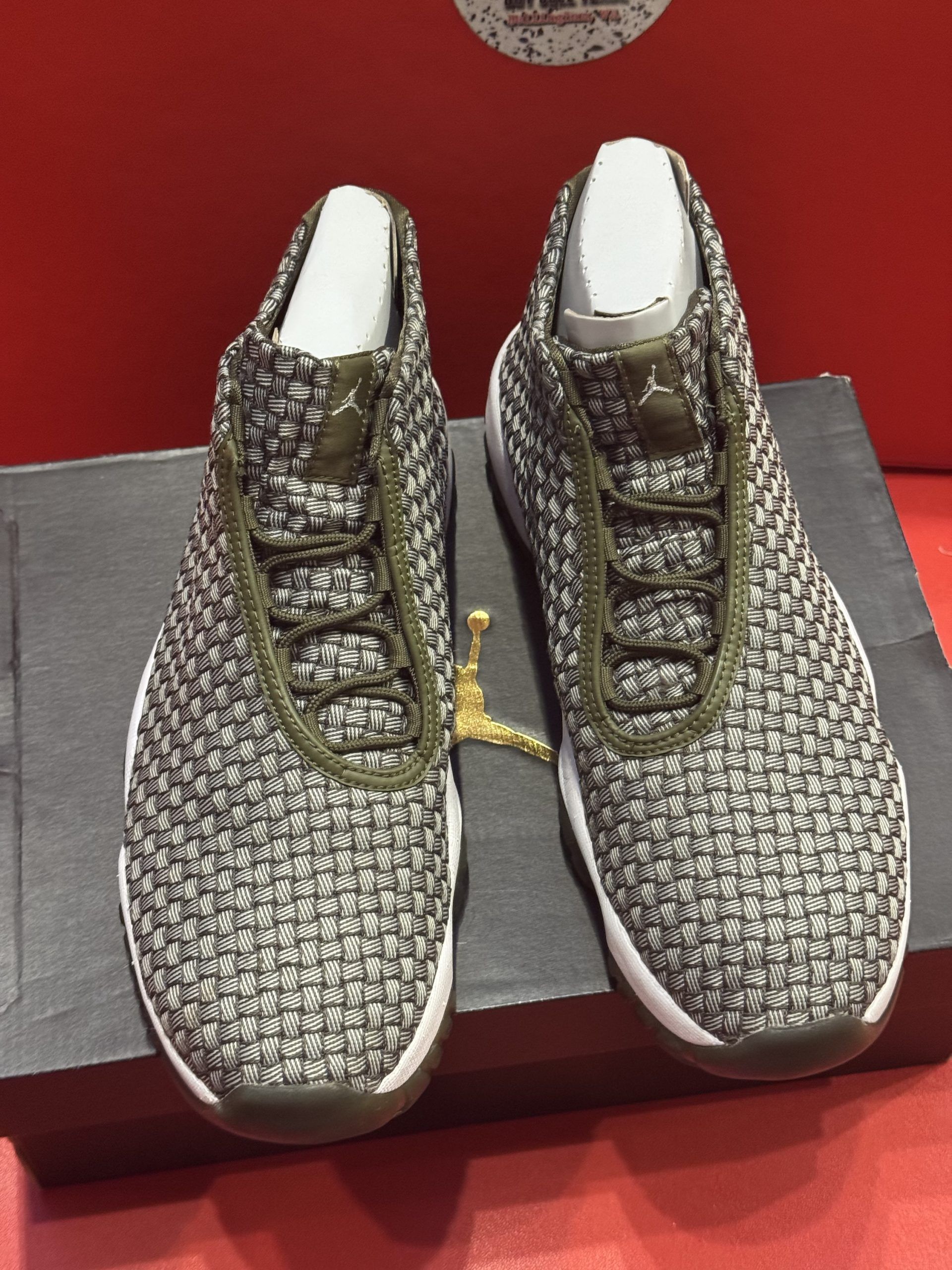 Pair of woven-pattern sneakers, olive green sole and trim, sitting on a black shoebox, against a red background.