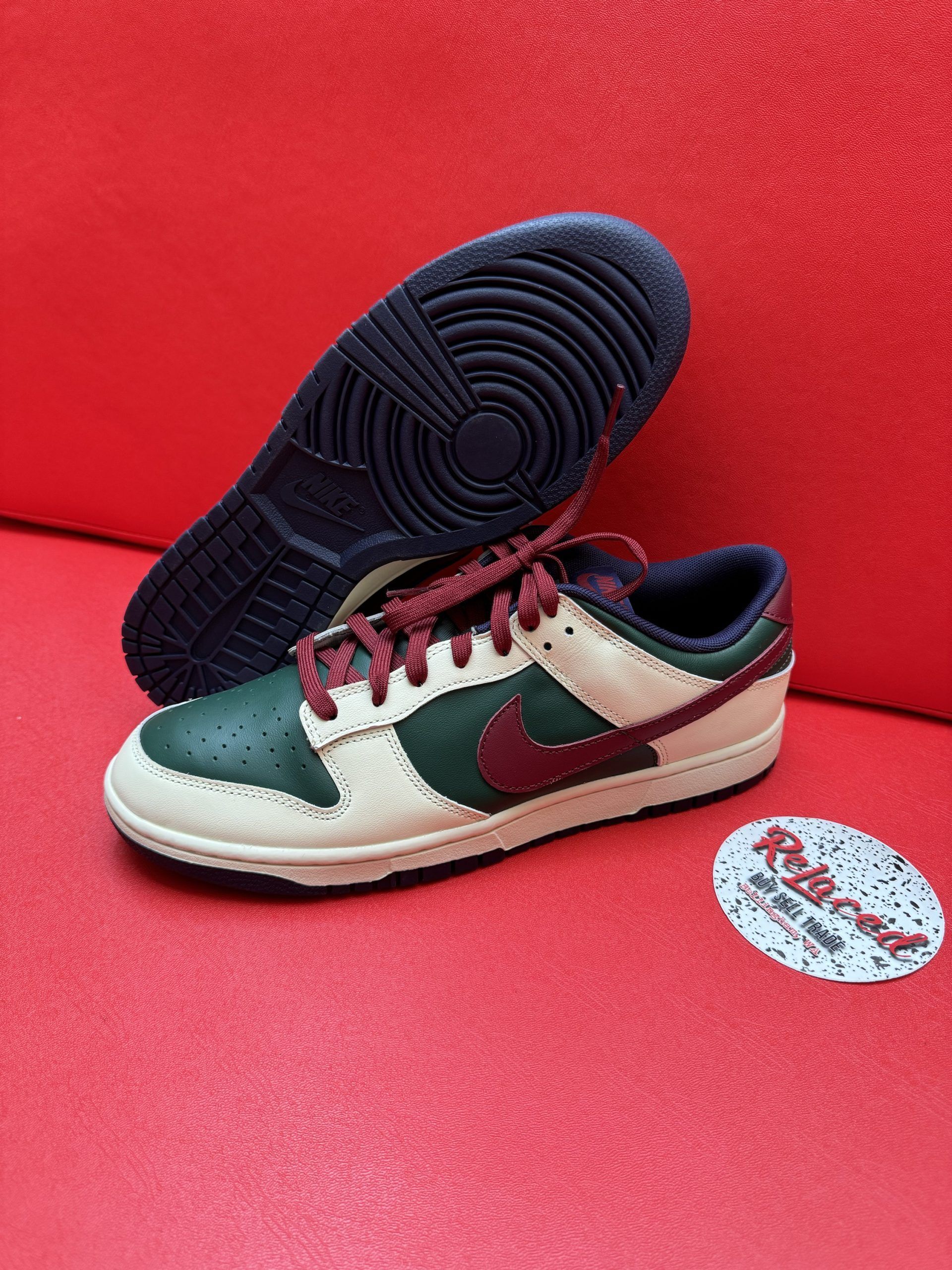 Nike Dunk Low sneakers with green, burgundy, and tan color scheme on red surface.