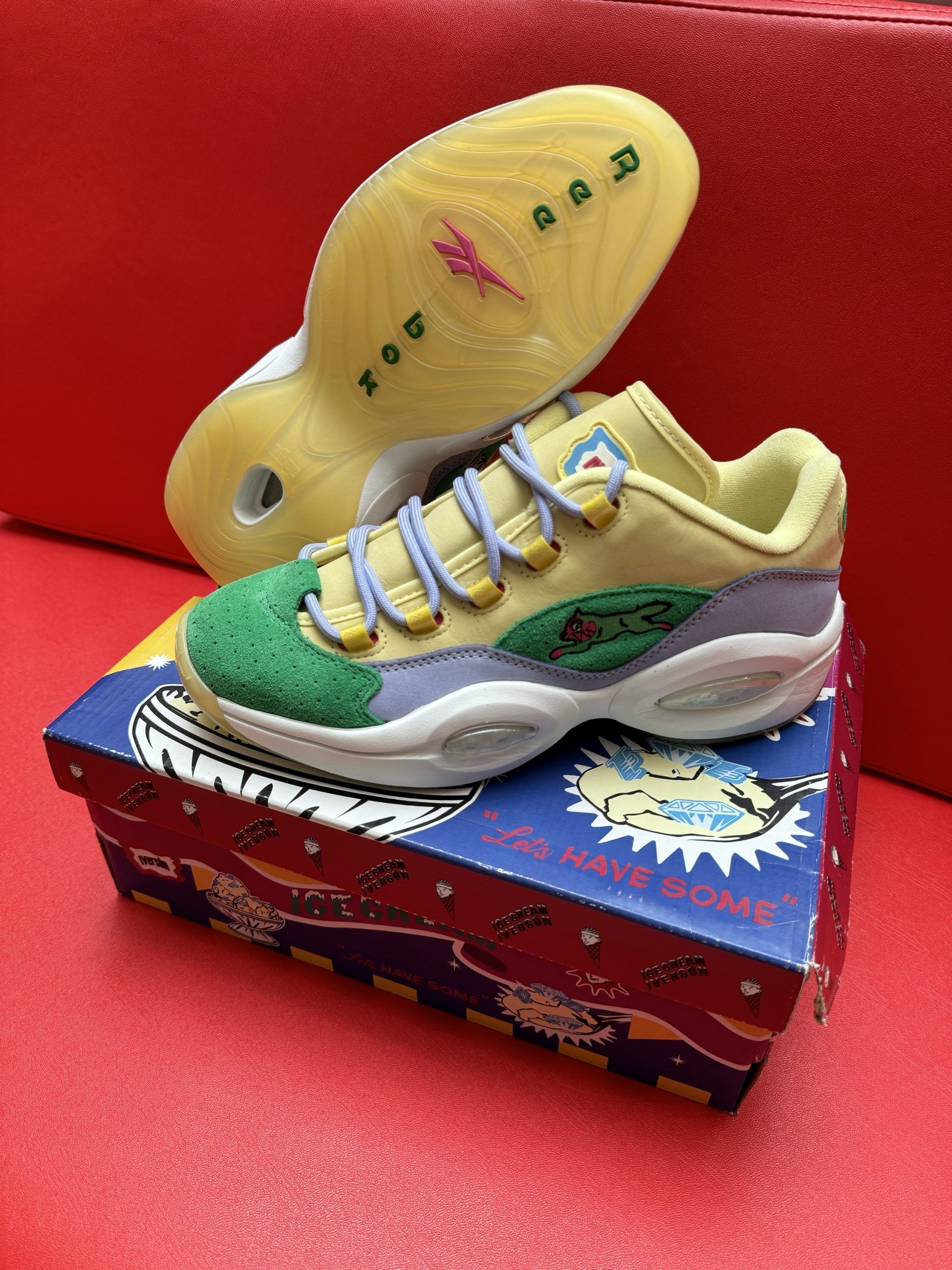 Reebok Question Low sneakers, colorful with green toe, sitting on a cartoon-decorated box, sole visible.