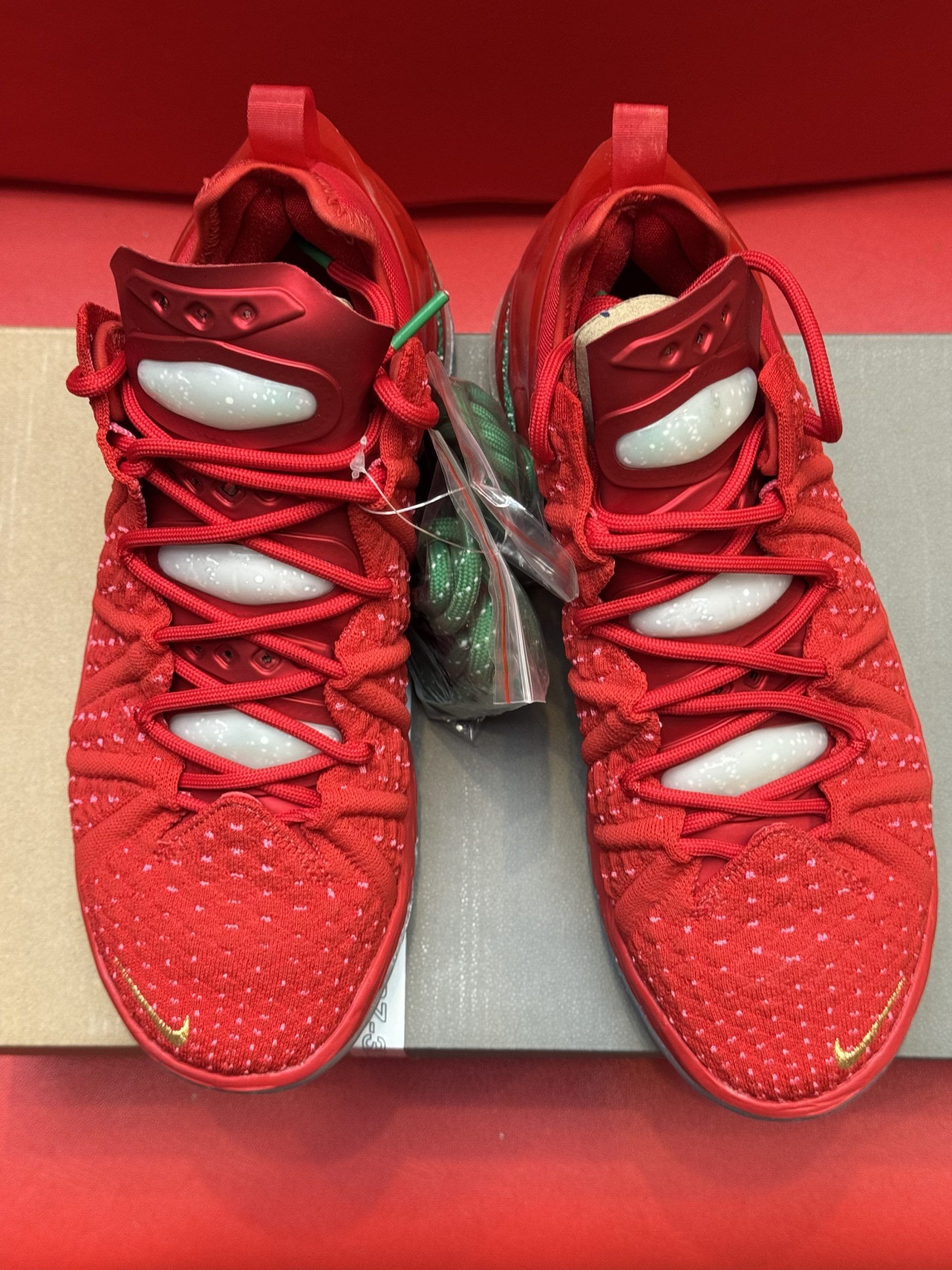Red Nike LeBron 18 basketball sneakers with white soles, placed atop a shoebox.