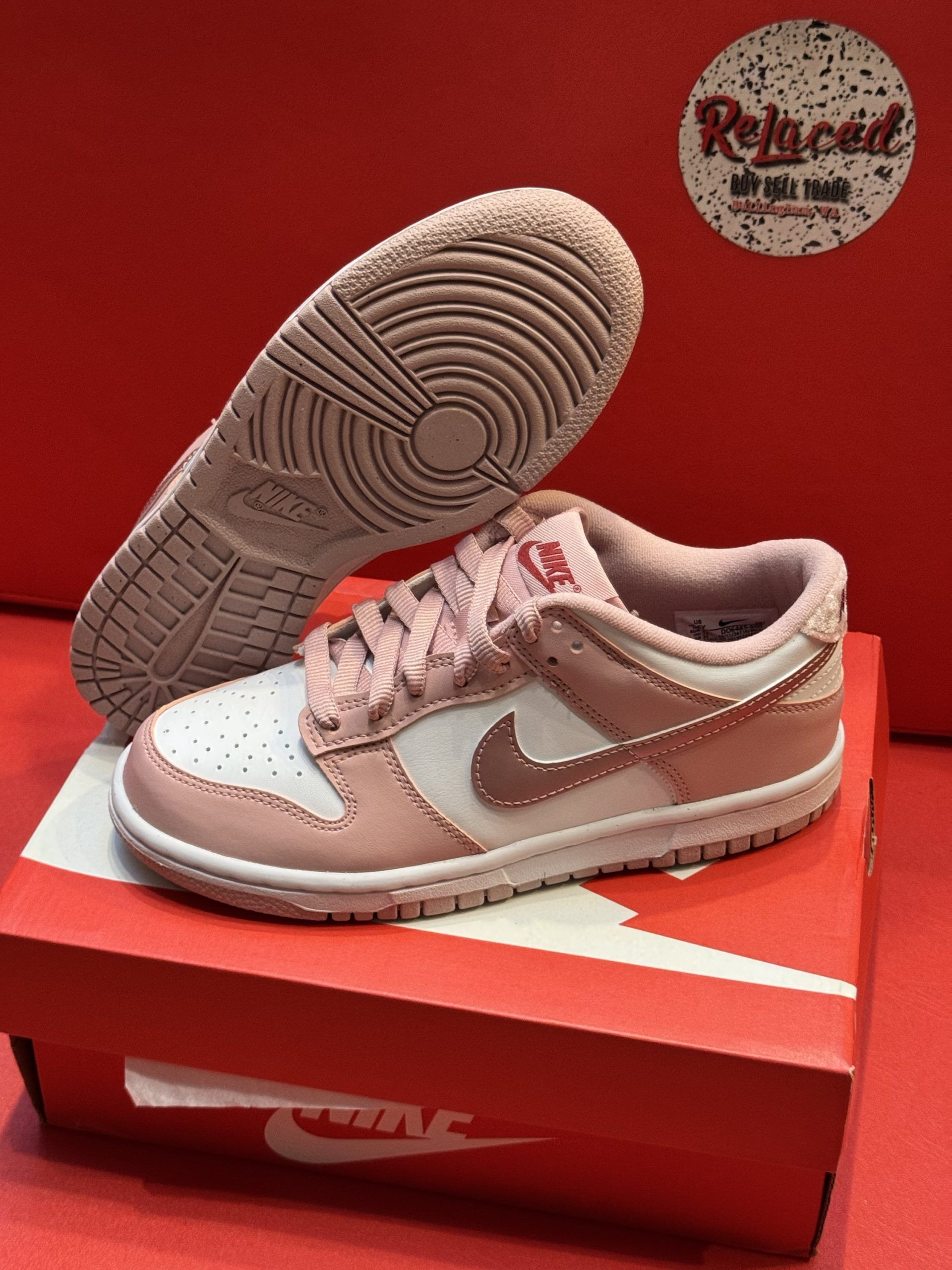 Pink and white Nike Dunk Low sneakers, one on the shoe box, sole up.