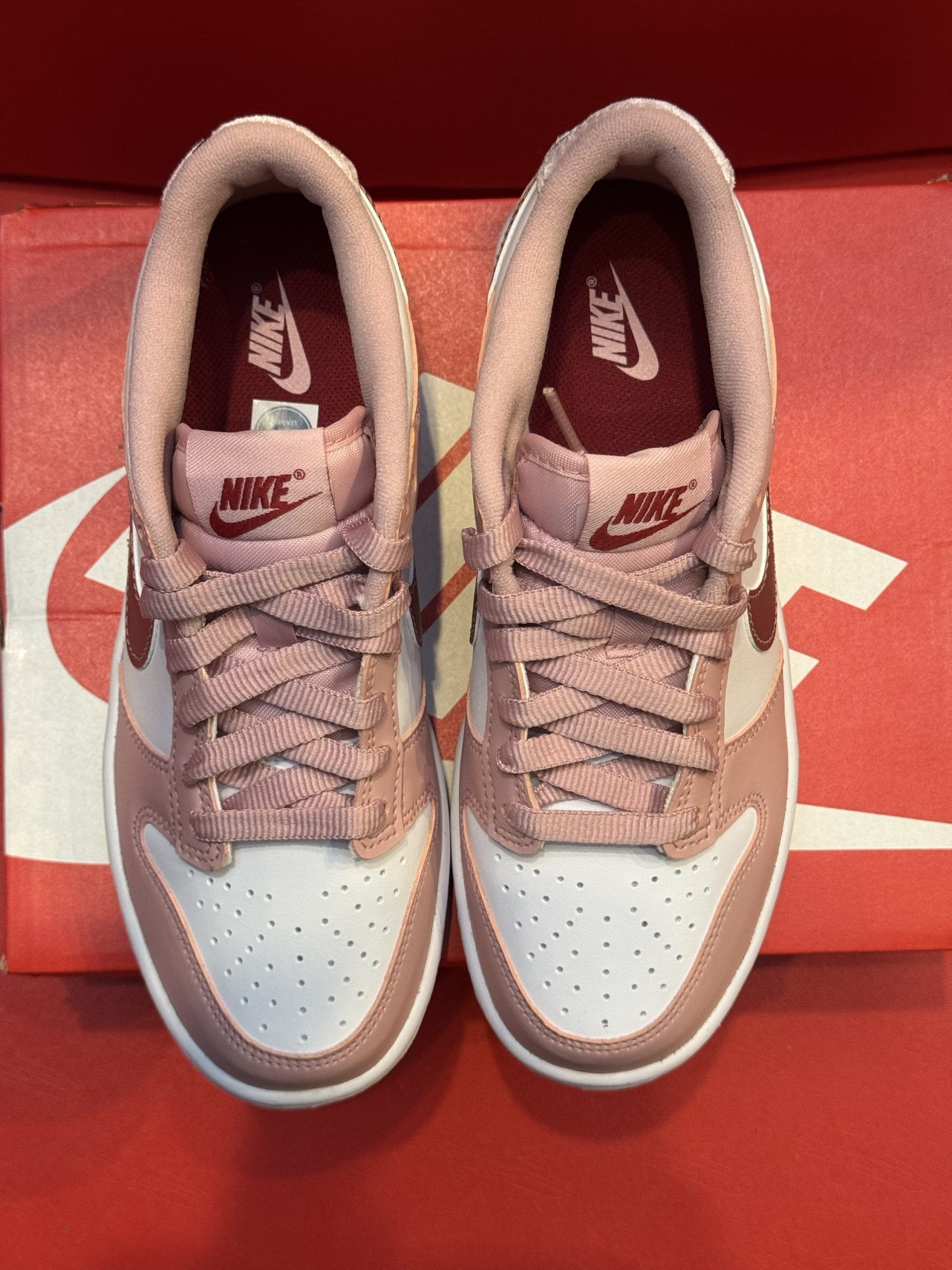 Pink and white Nike Dunk Low sneakers, one on the shoe box, sole up.