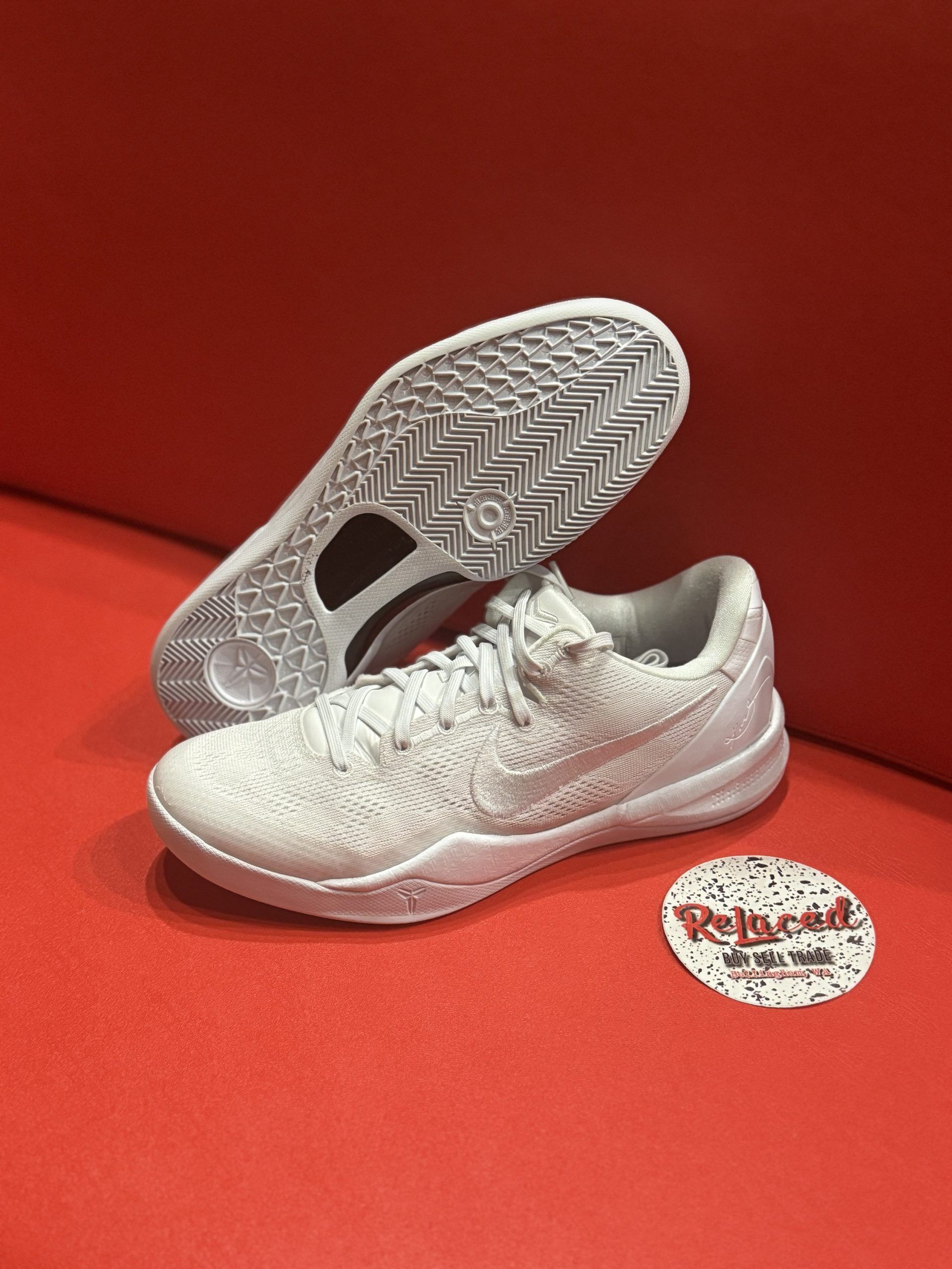 White Nike sneakers on a red surface, sole facing up.