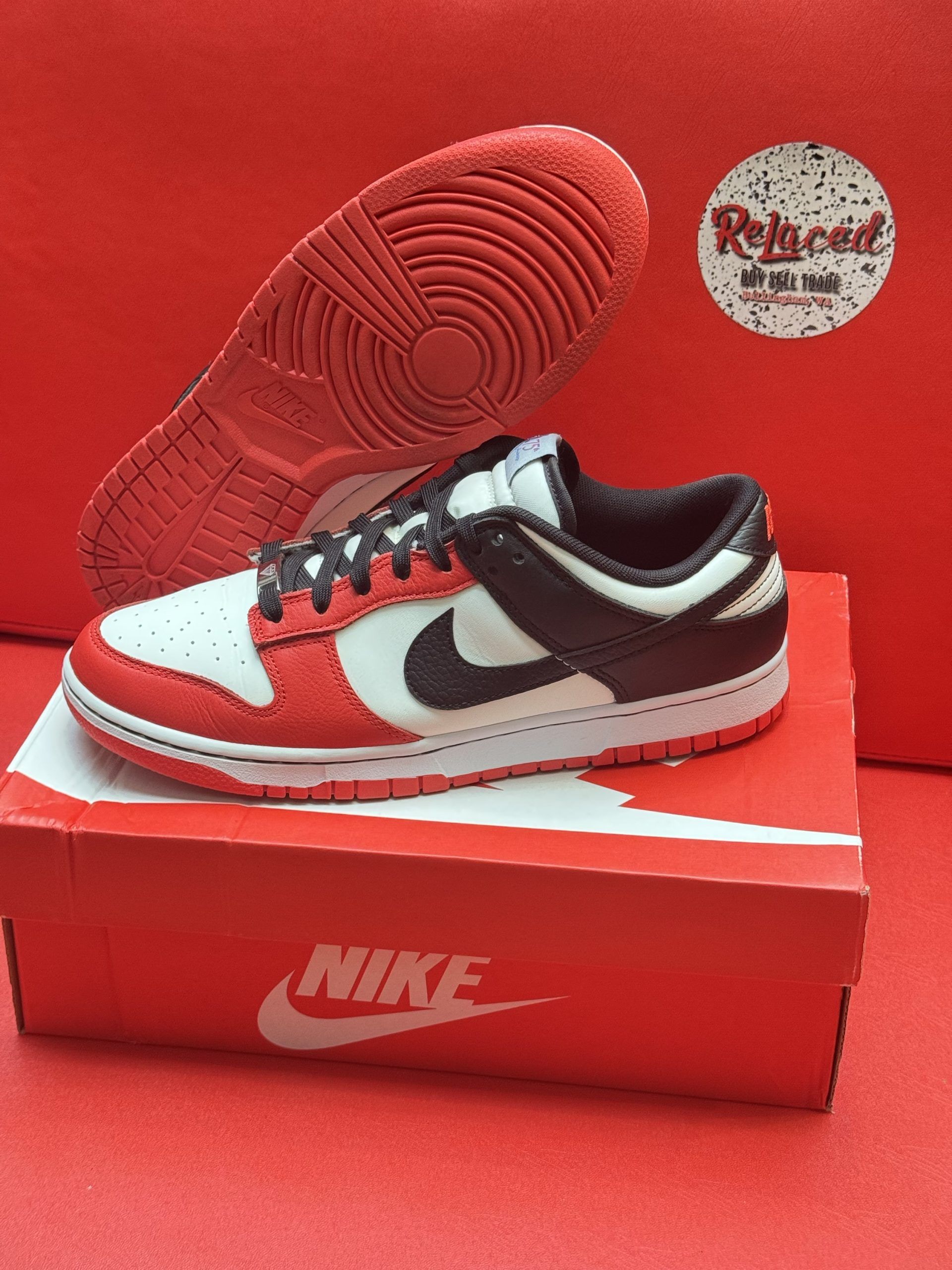 Red and white Nike Dunk Low shoe, black swoosh, on red Nike box with a matching sole, red background.
