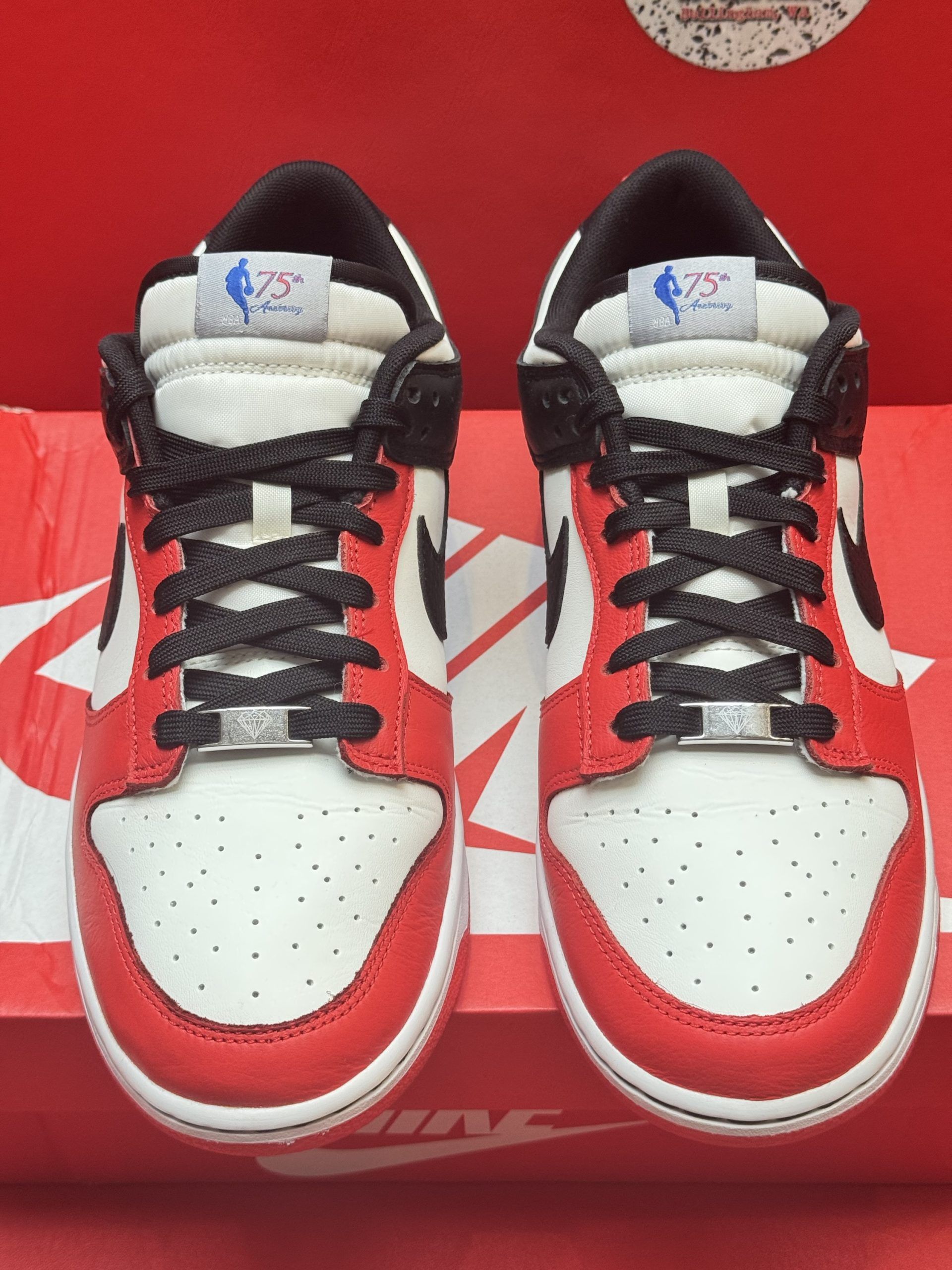 Red and white Nike Dunk Low shoe, black swoosh, on red Nike box with a matching sole, red background.