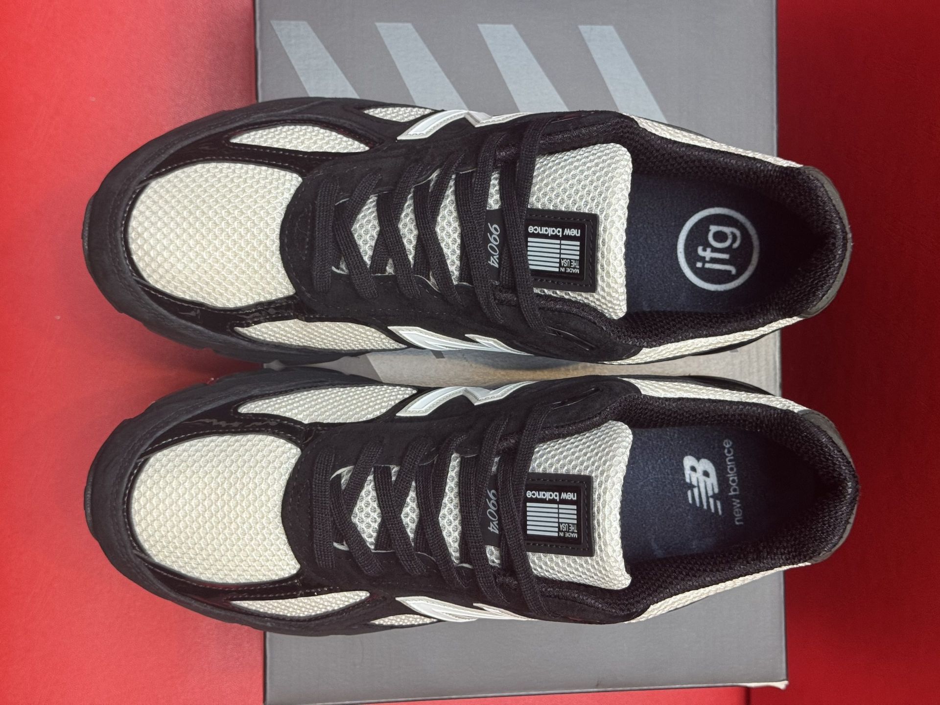 Black and cream New Balance sneakers on a black box, sole visible.