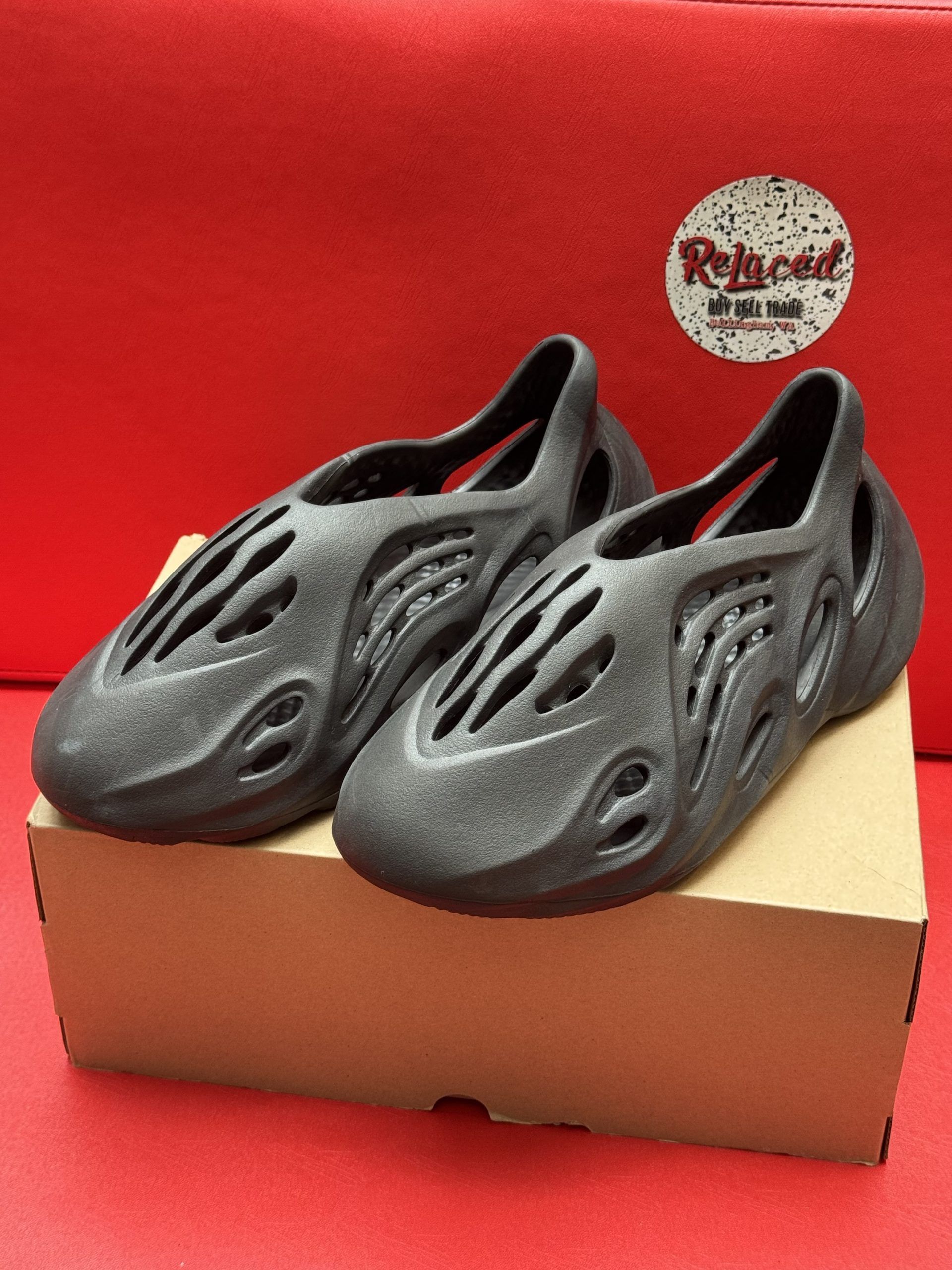 Pair of dark gray foam clogs on a cardboard box, set against a red background.